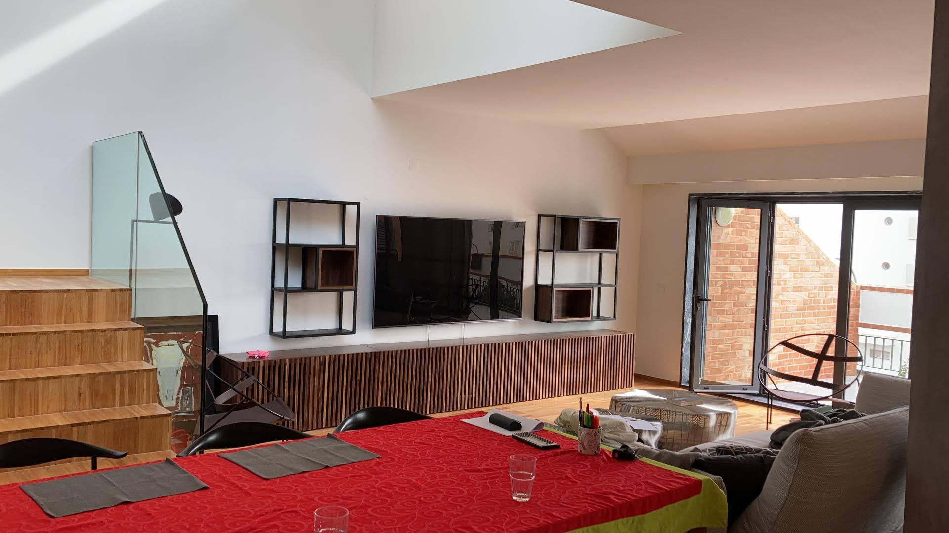 Sala open space com movel de TV em ripado de madeira escura, estantes metalicas pretas e mesa de jantar