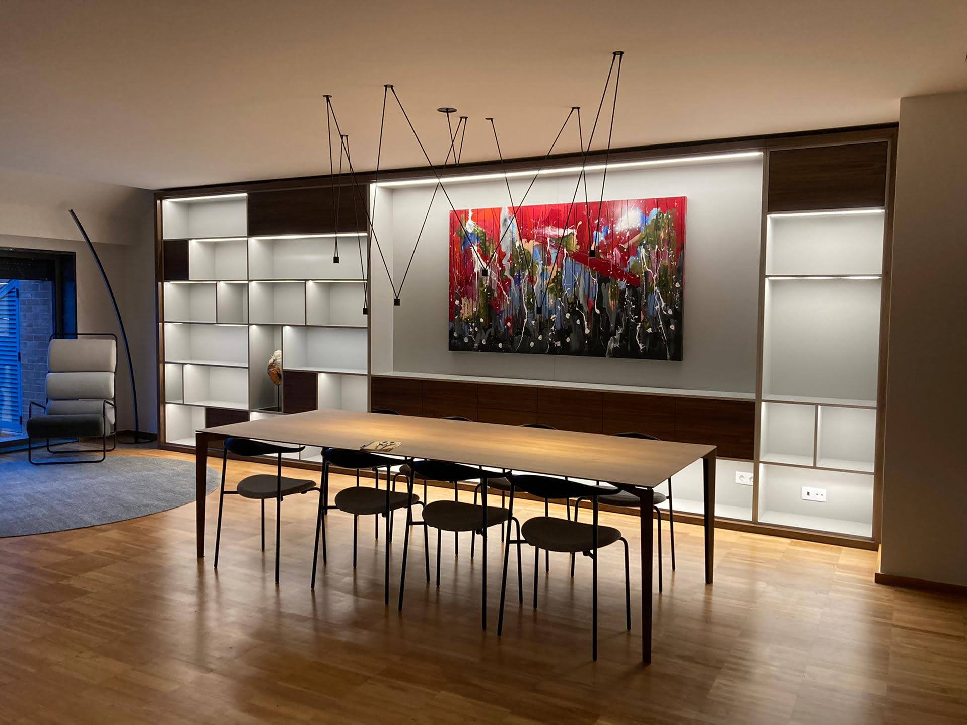 Sala de jantar com mesa em madeira e cadeiras pretas, estante embutida em lacado branco e nogueira com iluminacao LED