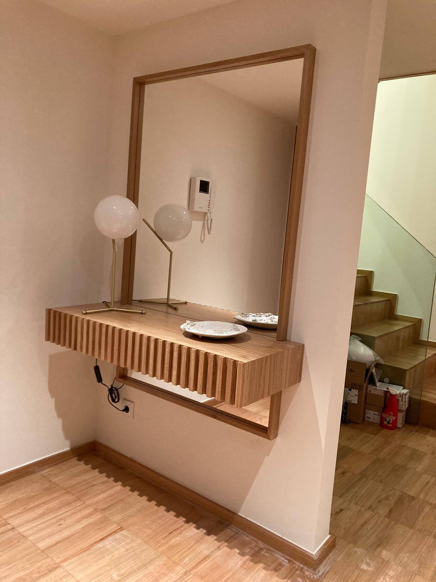 Hall com consola suspensa em ripado de madeira, espelho grande, candeeiro de vidro dourado e pavimento em parquet