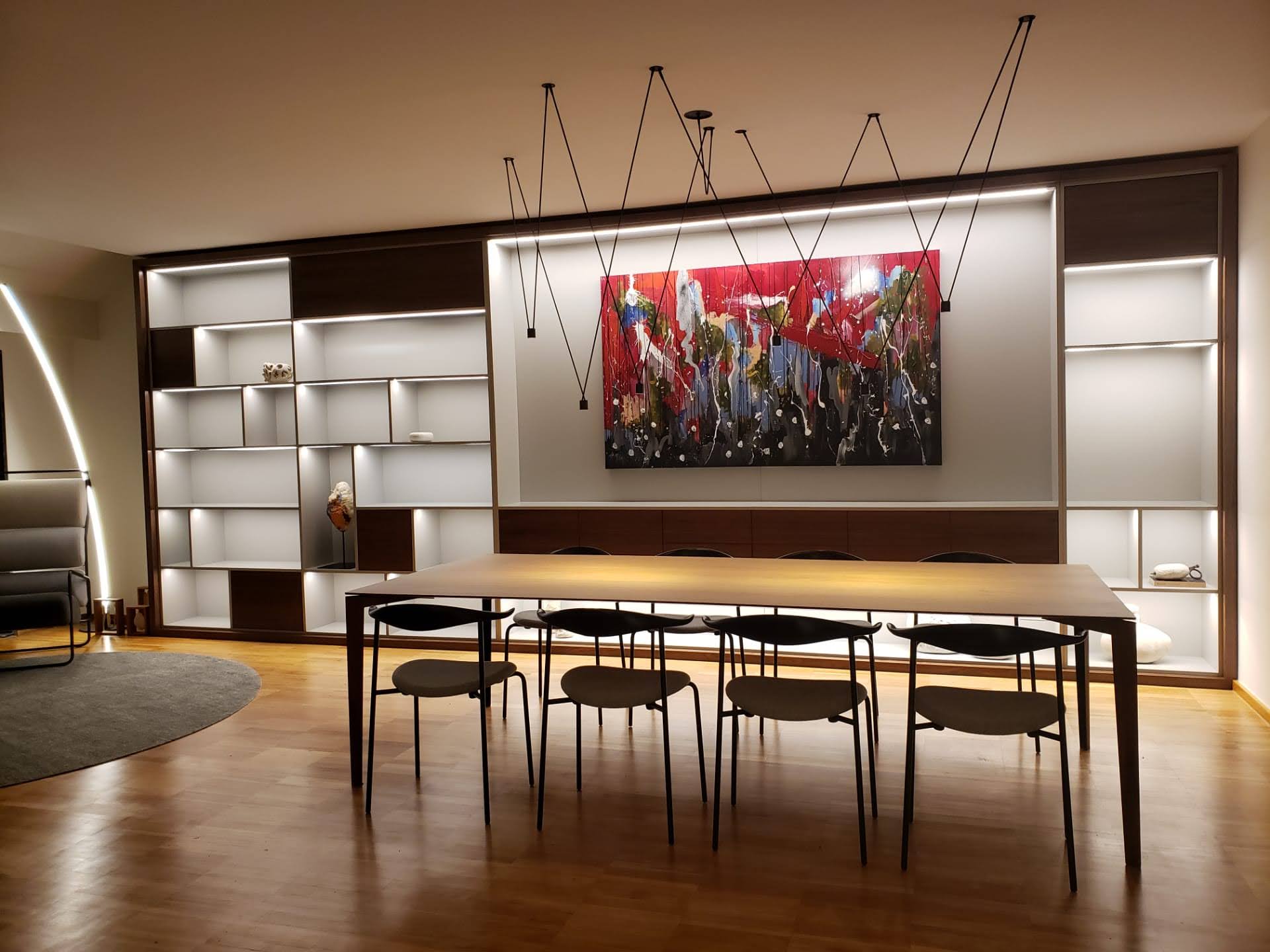 Sala de jantar com mesa em madeira, cadeiras de design, estante iluminada e candeeiros pendentes geometricos