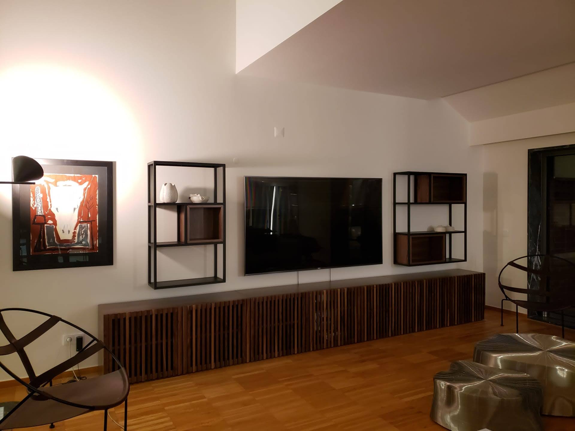 Sala com movel de TV extenso em ripado escuro, estantes metalicas, quadro emoldurado e pe-direito duplo