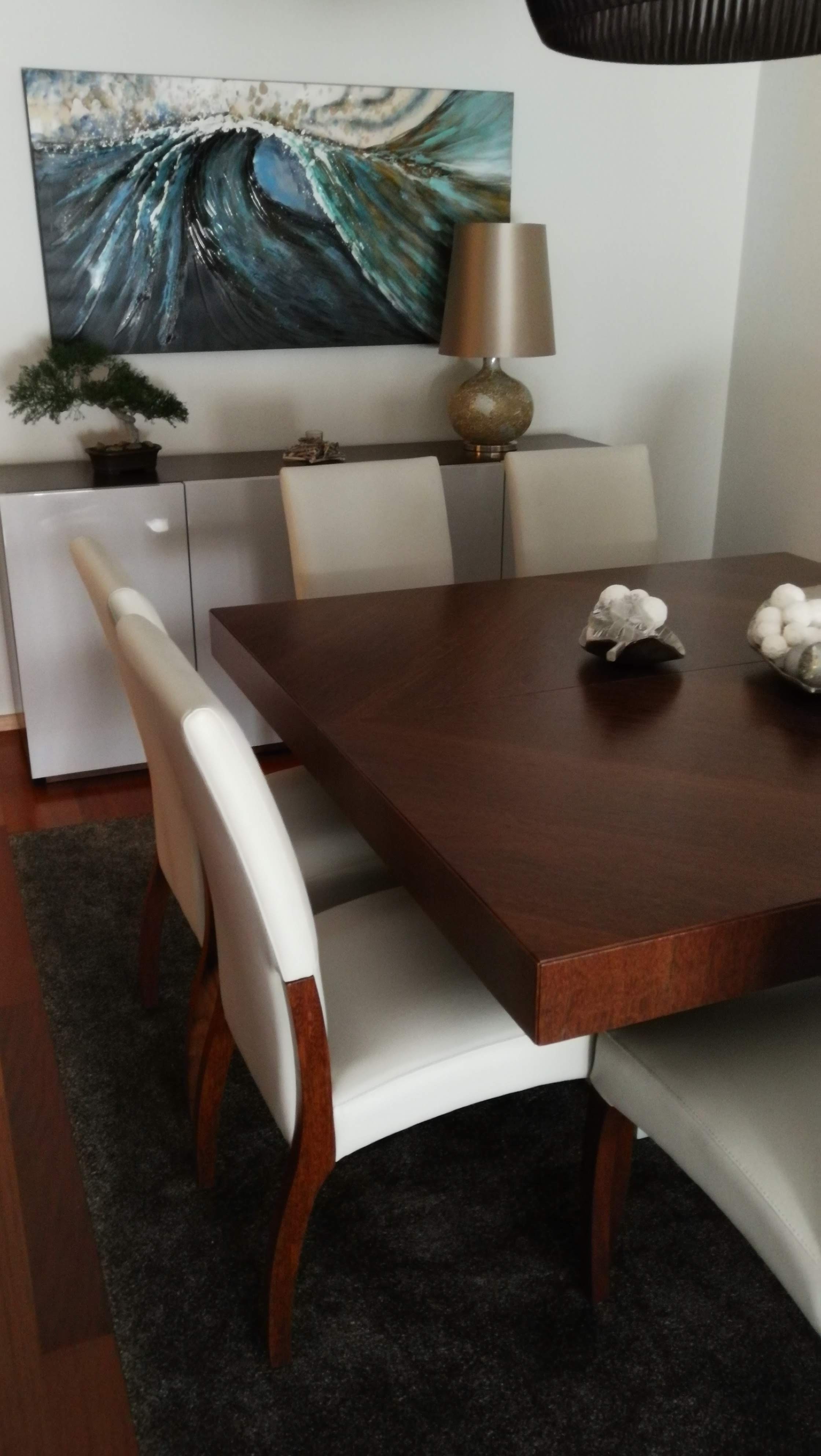 Sala de jantar com mesa em nogueira, cadeiras em pele branca, aparador cinza e quadro com motivo de onda do mar