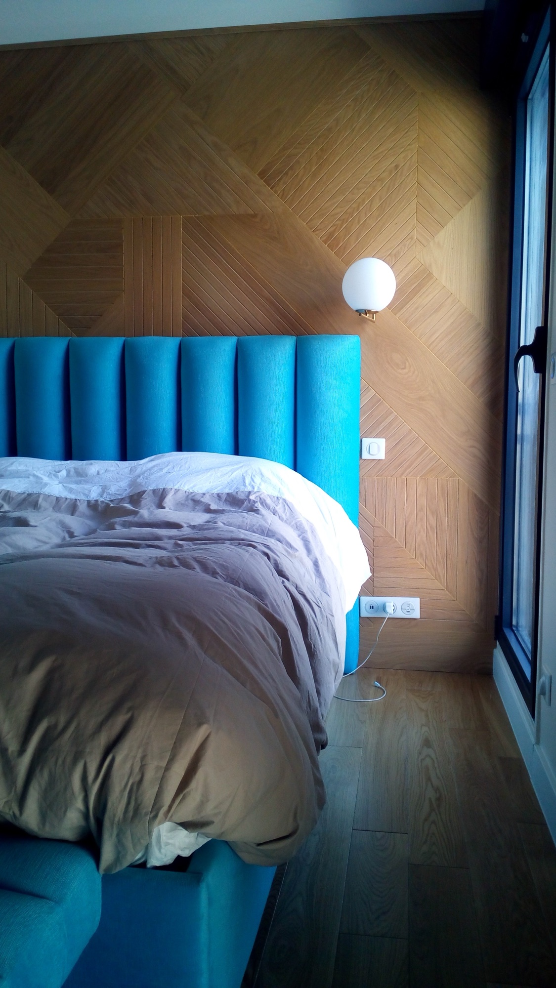 Quarto com cabeceira estofada azul-turquesa, parede em carvalho com padrao espinha e candeeiro esferica