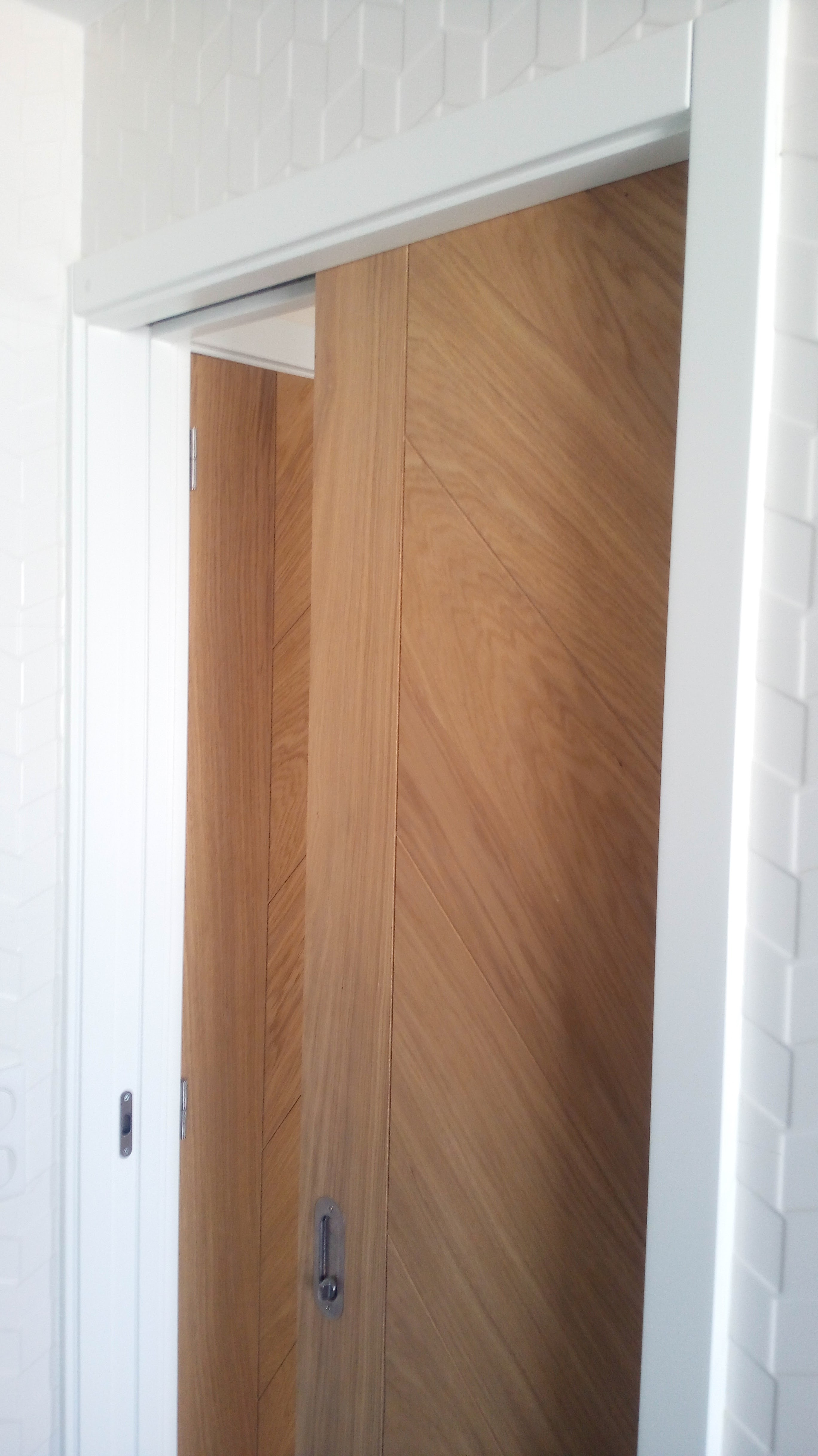 Porta de correr em carvalho com padrao chevron embutida na parede com azulejo tridimensional