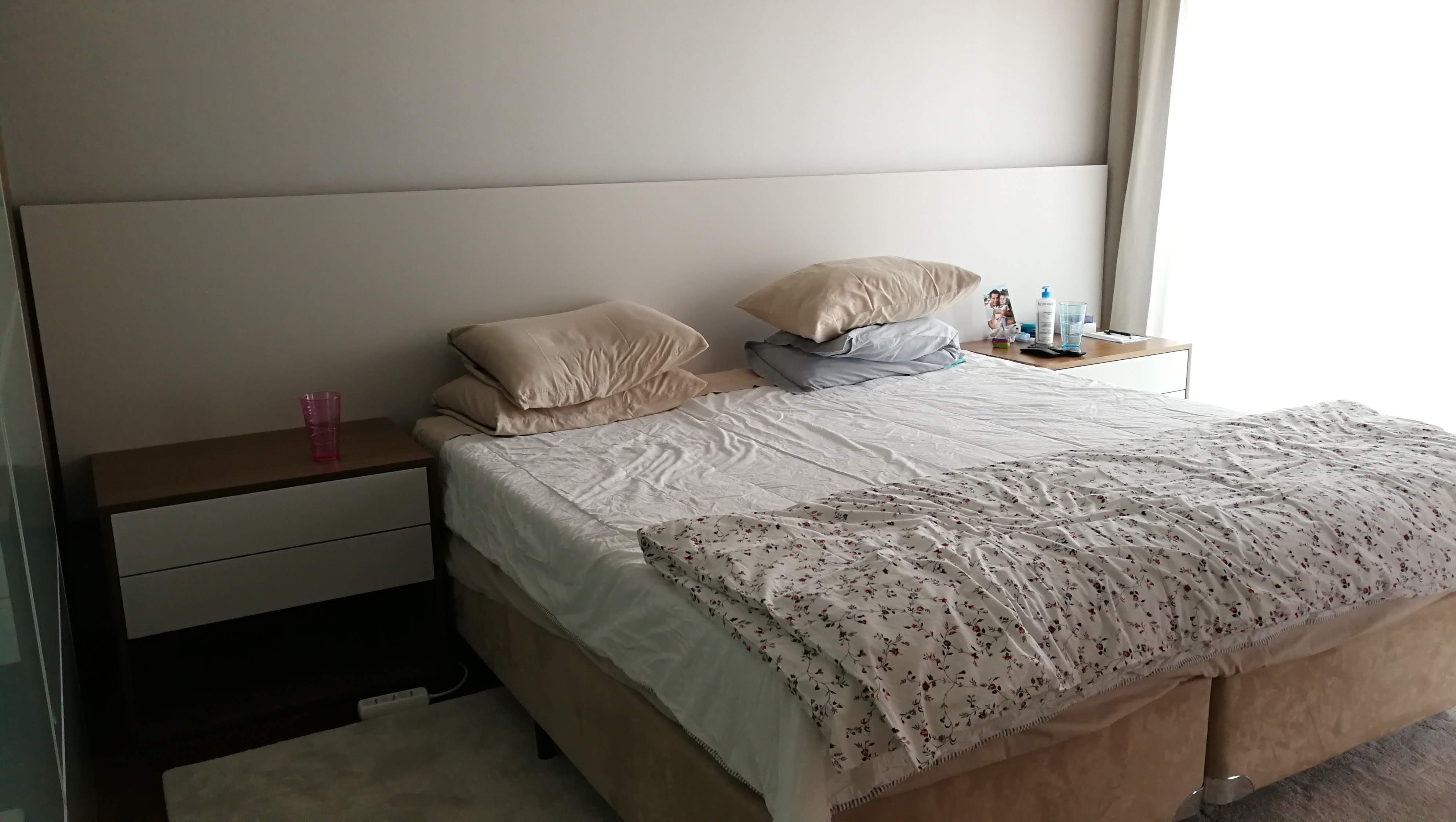 Quarto de casal com cama estofada bege, mesas de cabeceira em madeira e lacado branco