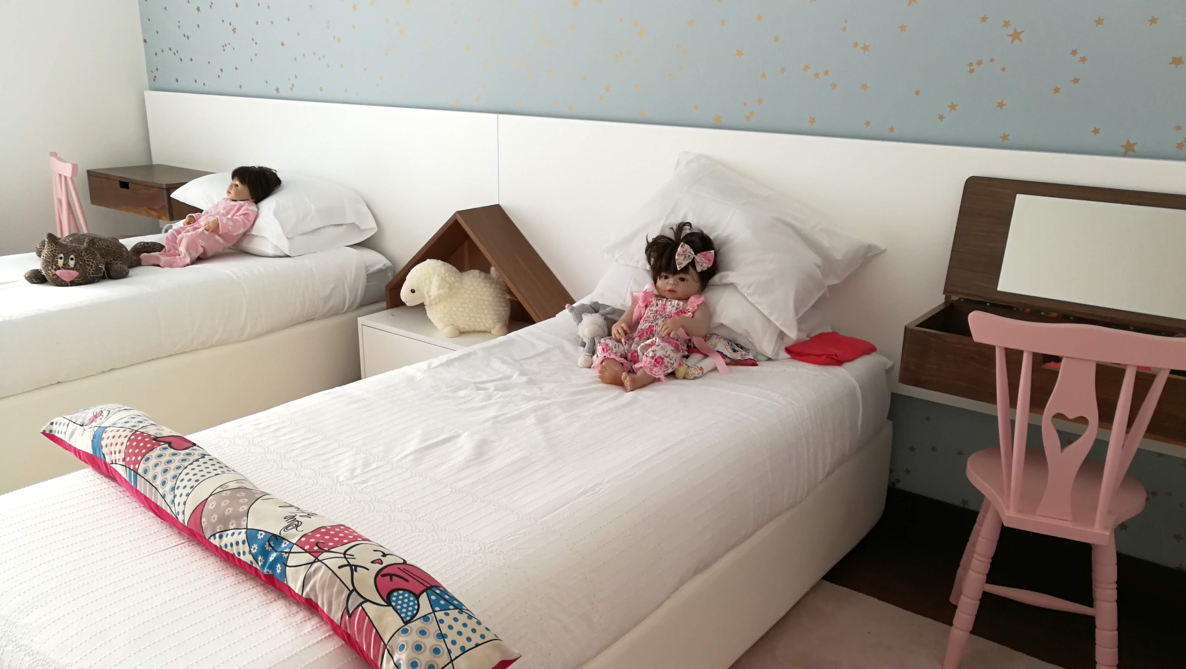 Quarto infantil com camas individuais brancas, papel de parede azul com estrelas douradas e mesa casinha