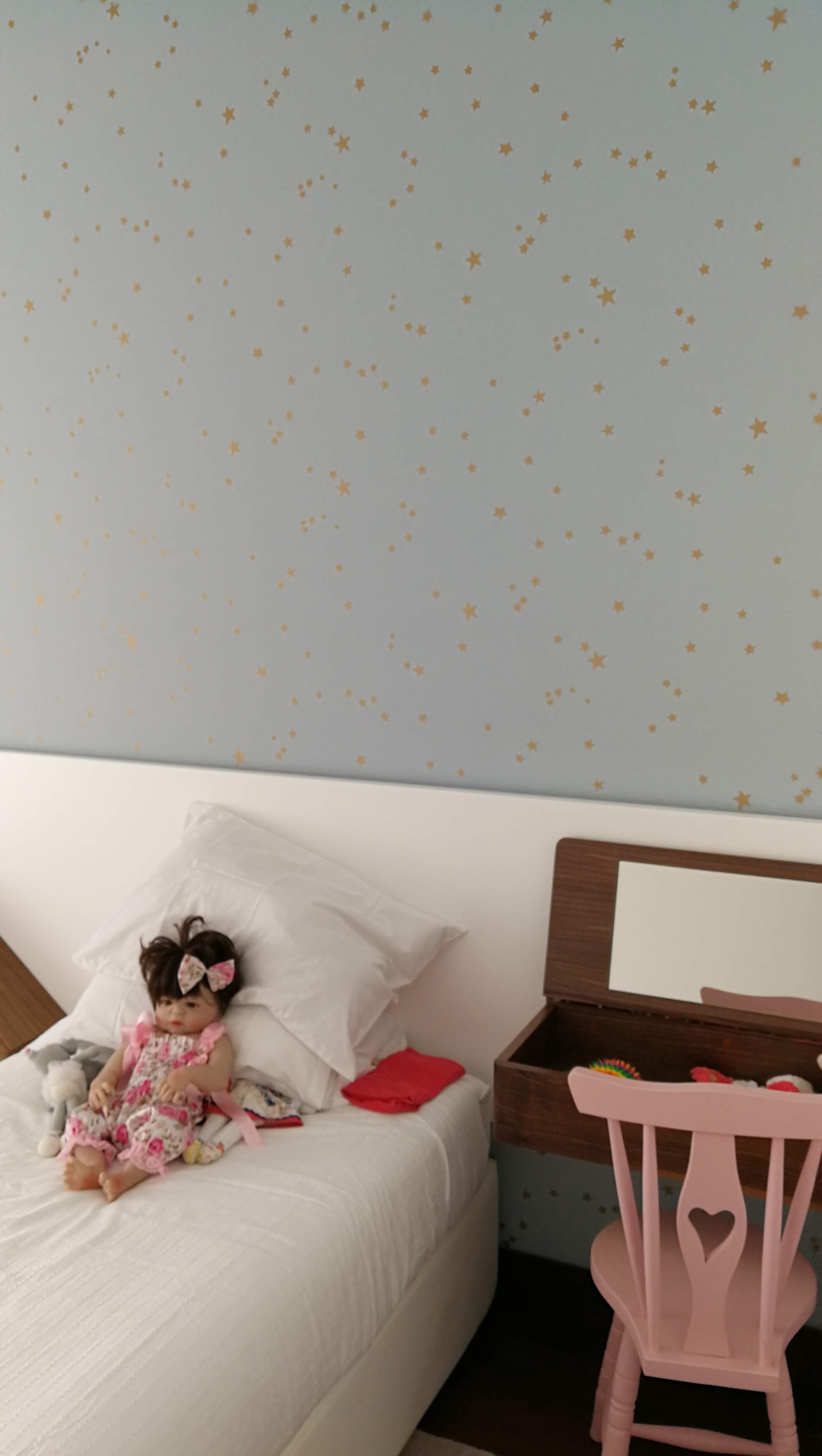 Quarto infantil com cama branca, papel de parede azul com estrelas e mesa de cabeceira em nogueira