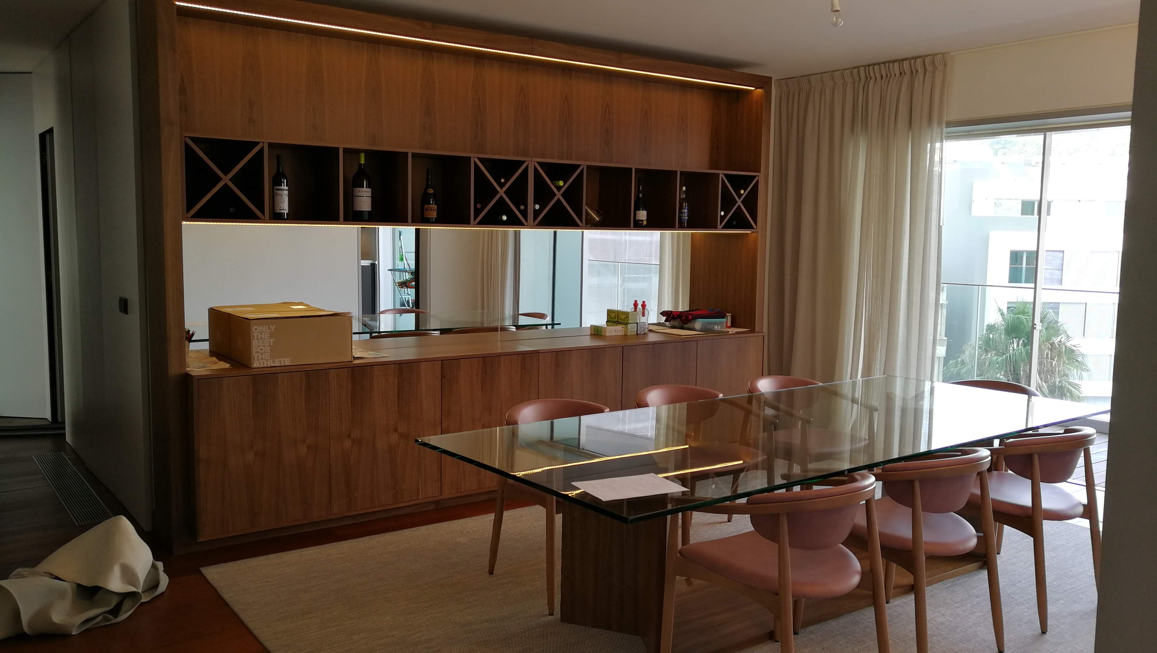 Sala de jantar com aparador em nogueira com garrafeira e espelho, mesa em vidro e cadeiras rosa