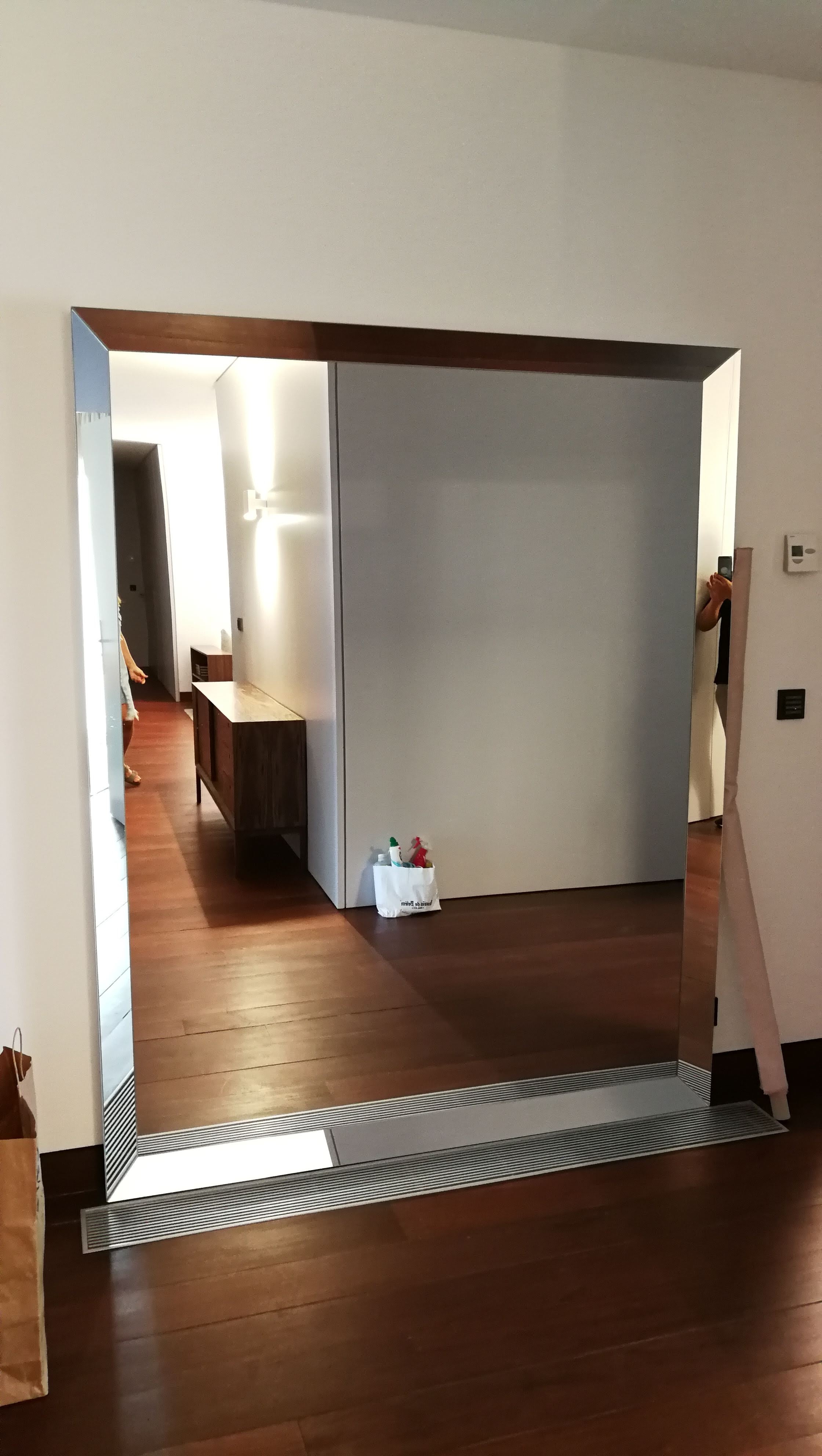 Espelho grande com moldura em nogueira apoiado no chao em pavimento de madeira escura