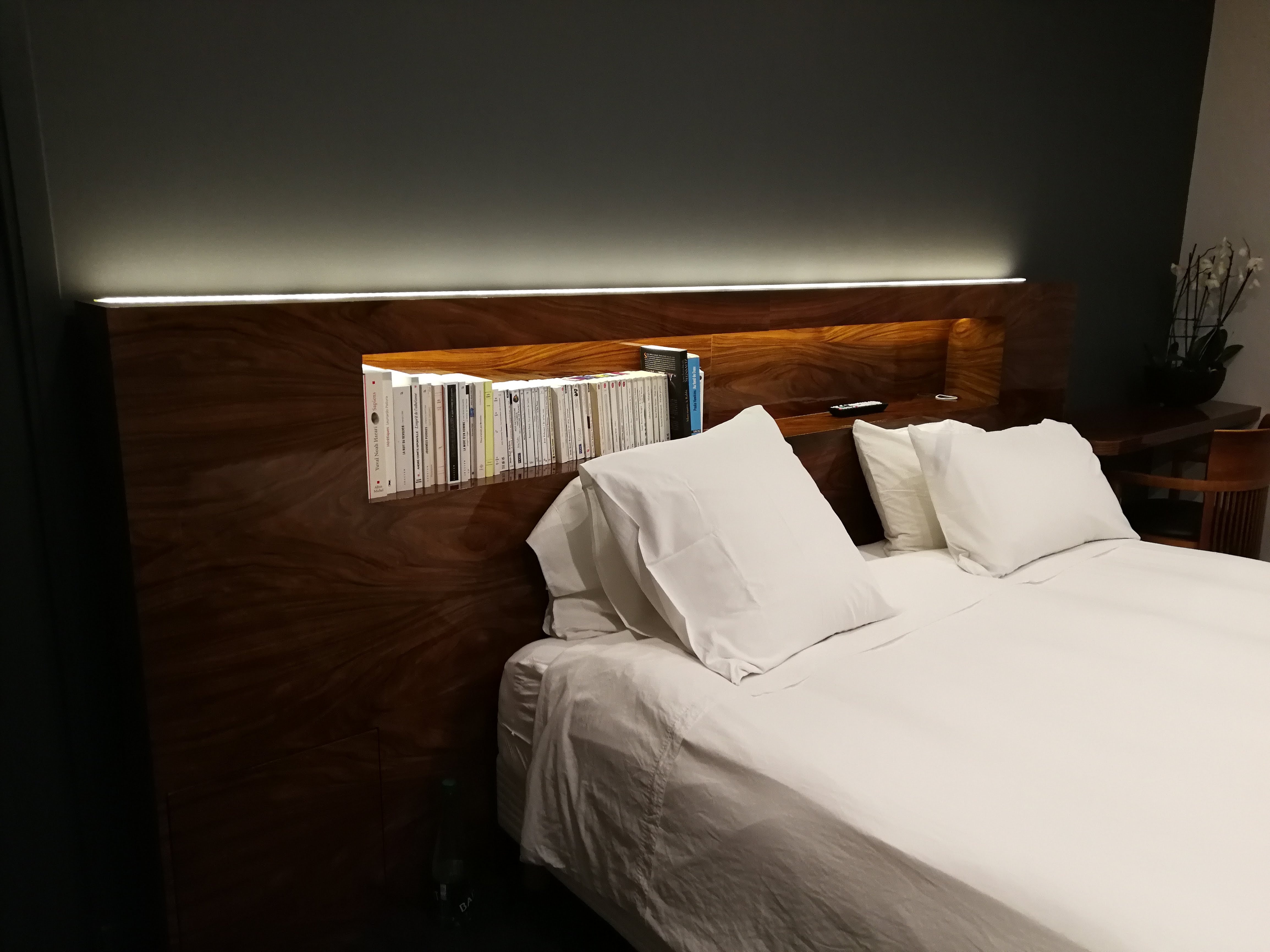 Cabeceira em nogueira com prateleira iluminada por LED, roupa de cama branca e parede cinza escuro