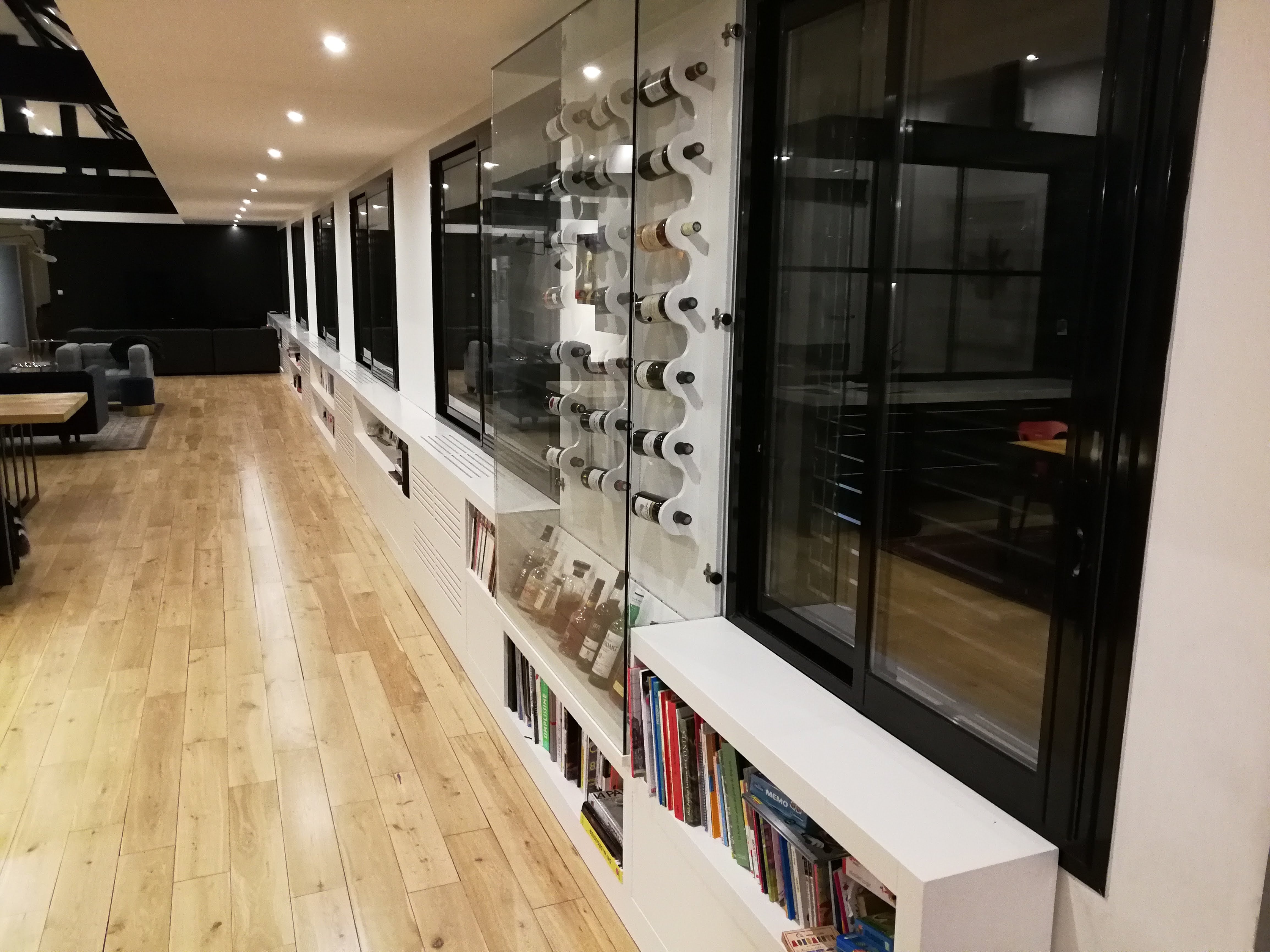 Corredor com garrafeira em vidro e estrutura branca, prateleiras com livros e pavimento em carvalho