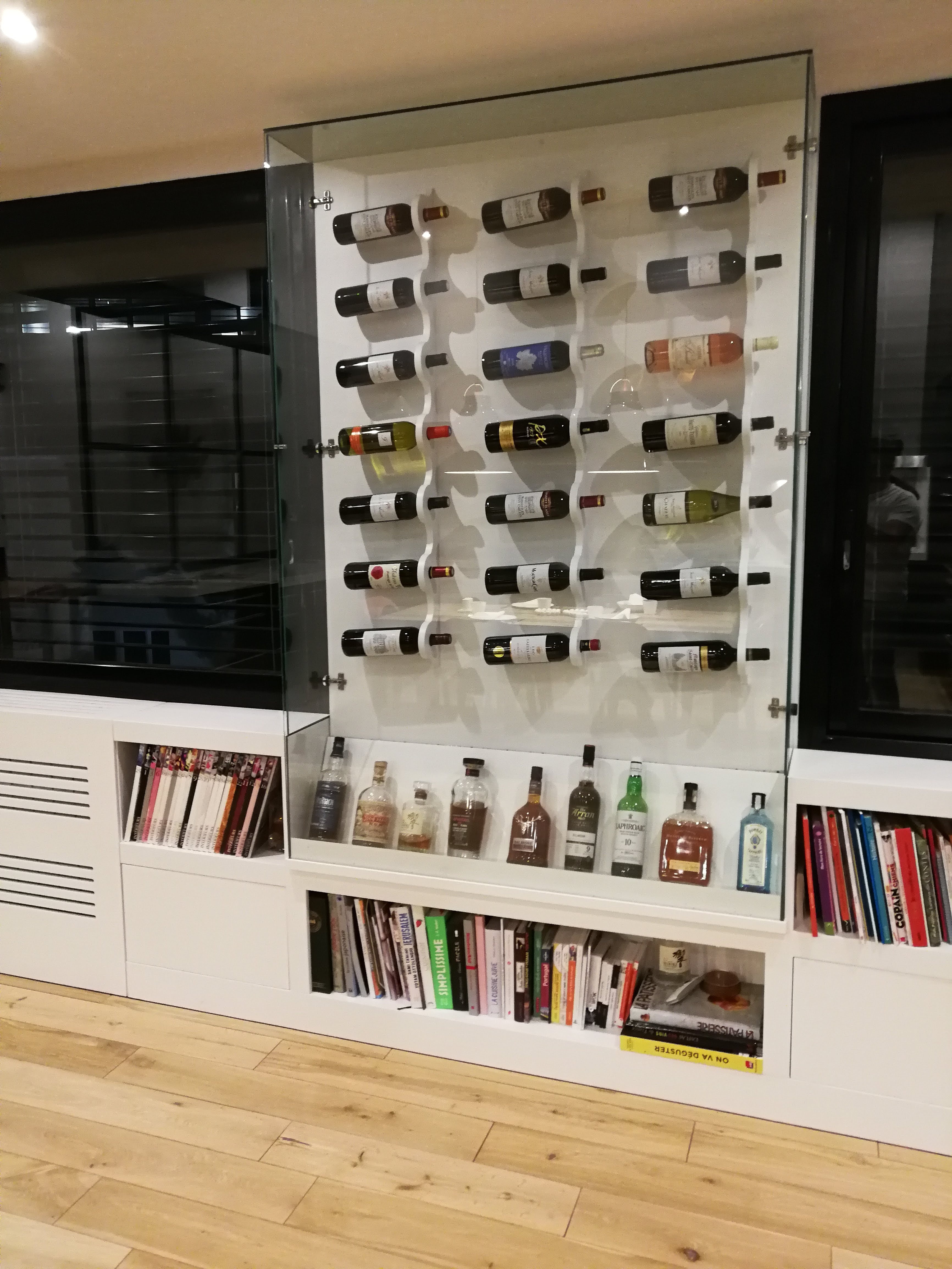 Garrafeira em vidro com suportes ondulados brancos, prateleiras com livros e bebidas