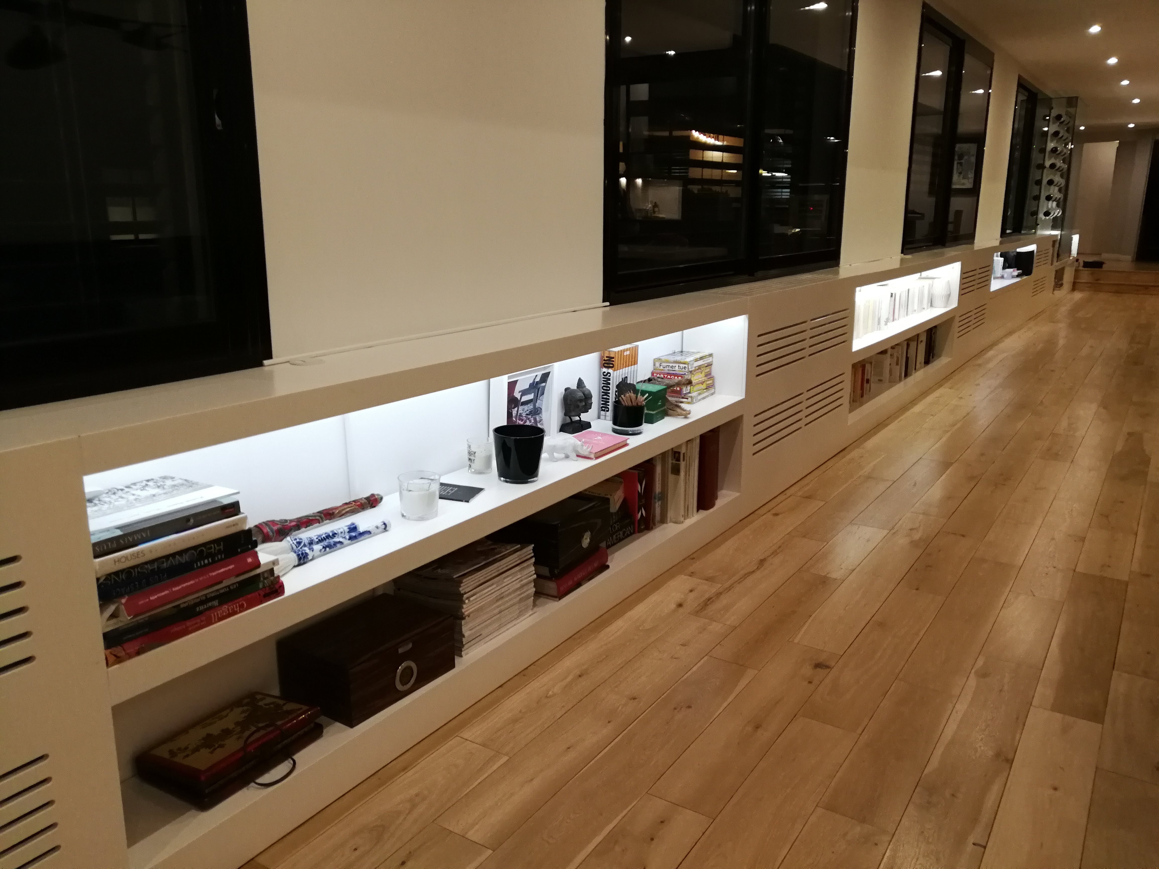 Movel baixo branco com prateleiras iluminadas, livros e objetos decorativos