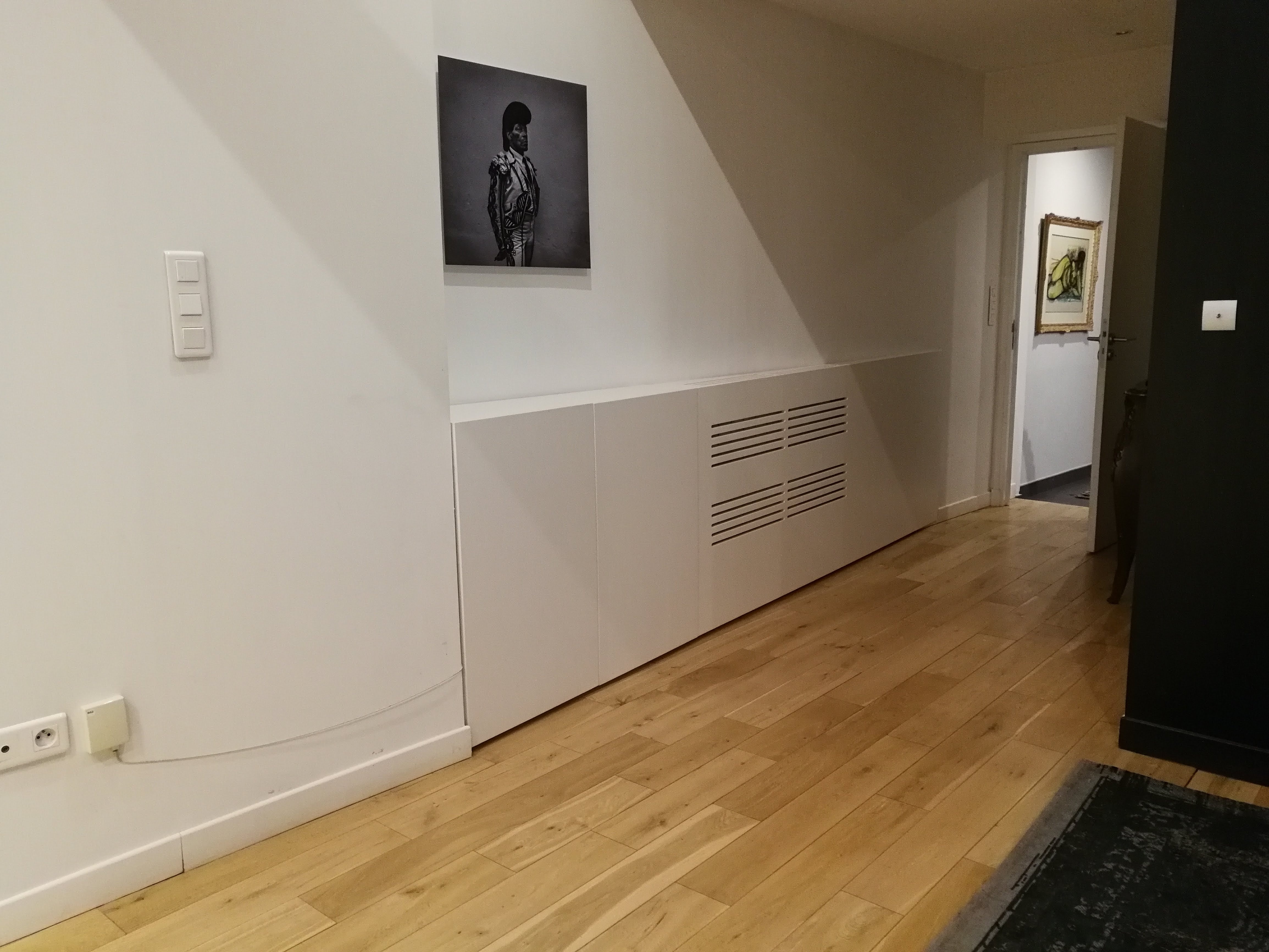 Corredor com movel baixo branco embutido sob parede inclinada e quadro a preto e branco