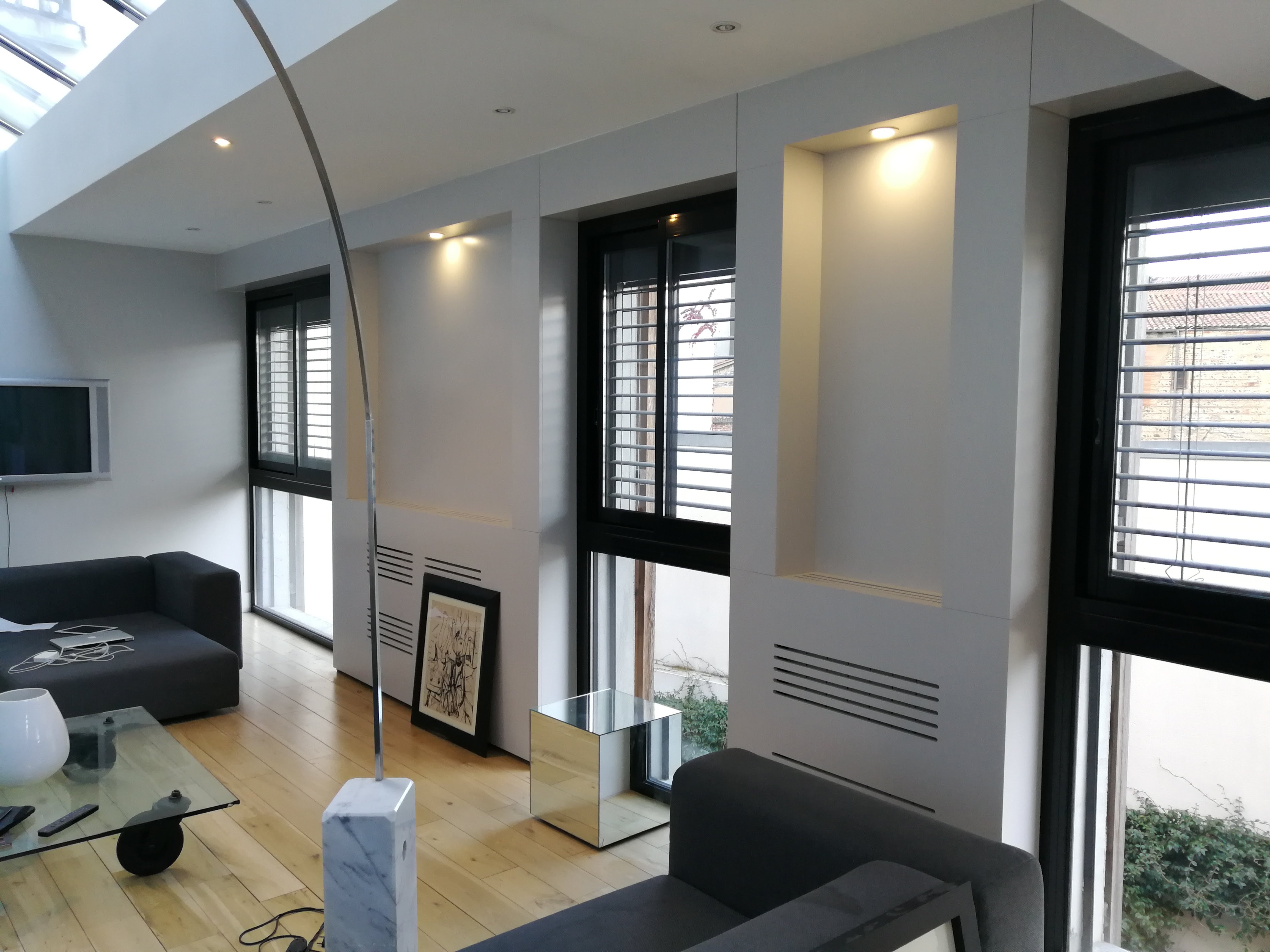 Sala ampla com pe-direito alto e claraboia, sofa cinza escuro, candeeiro em arco com base marmore