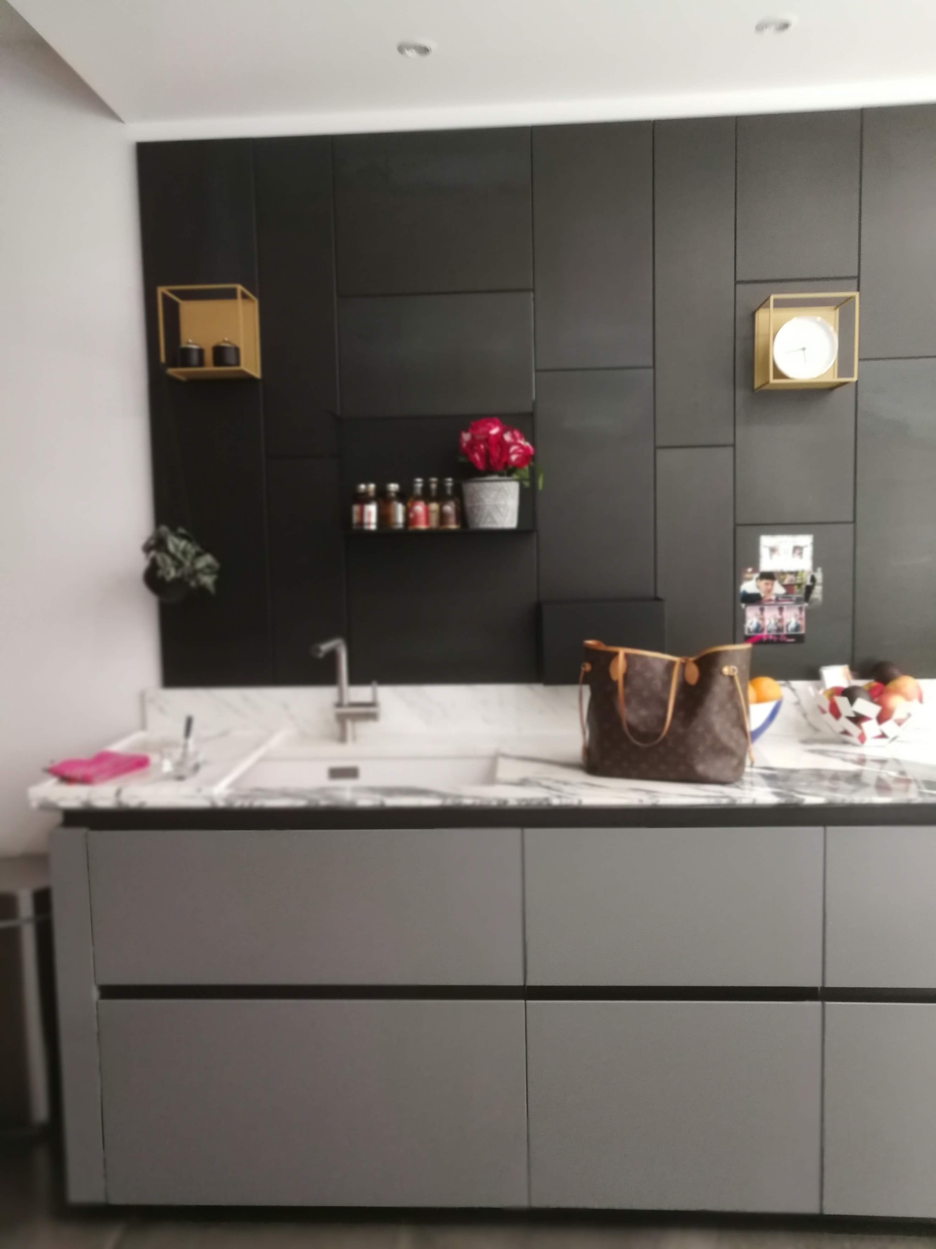 Bancada com lava-louca em marmore branco, armarios cinza e parede preta com prateleiras douradas