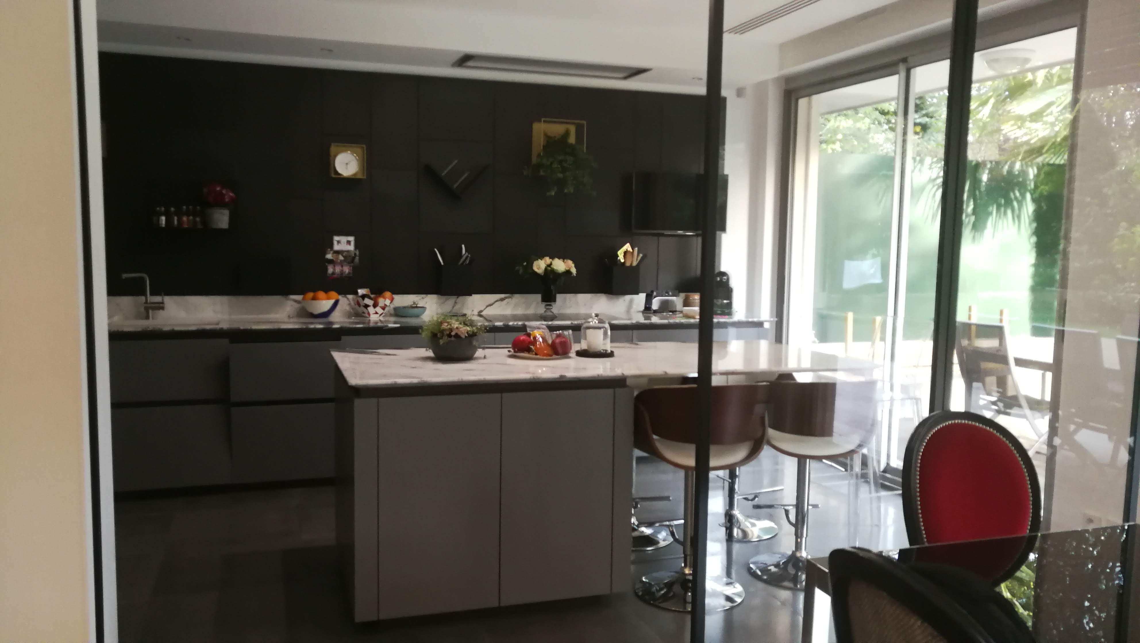 Cozinha ampla com ilha em marmore, parede preta com prateleiras douradas e portas de vidro para jardim