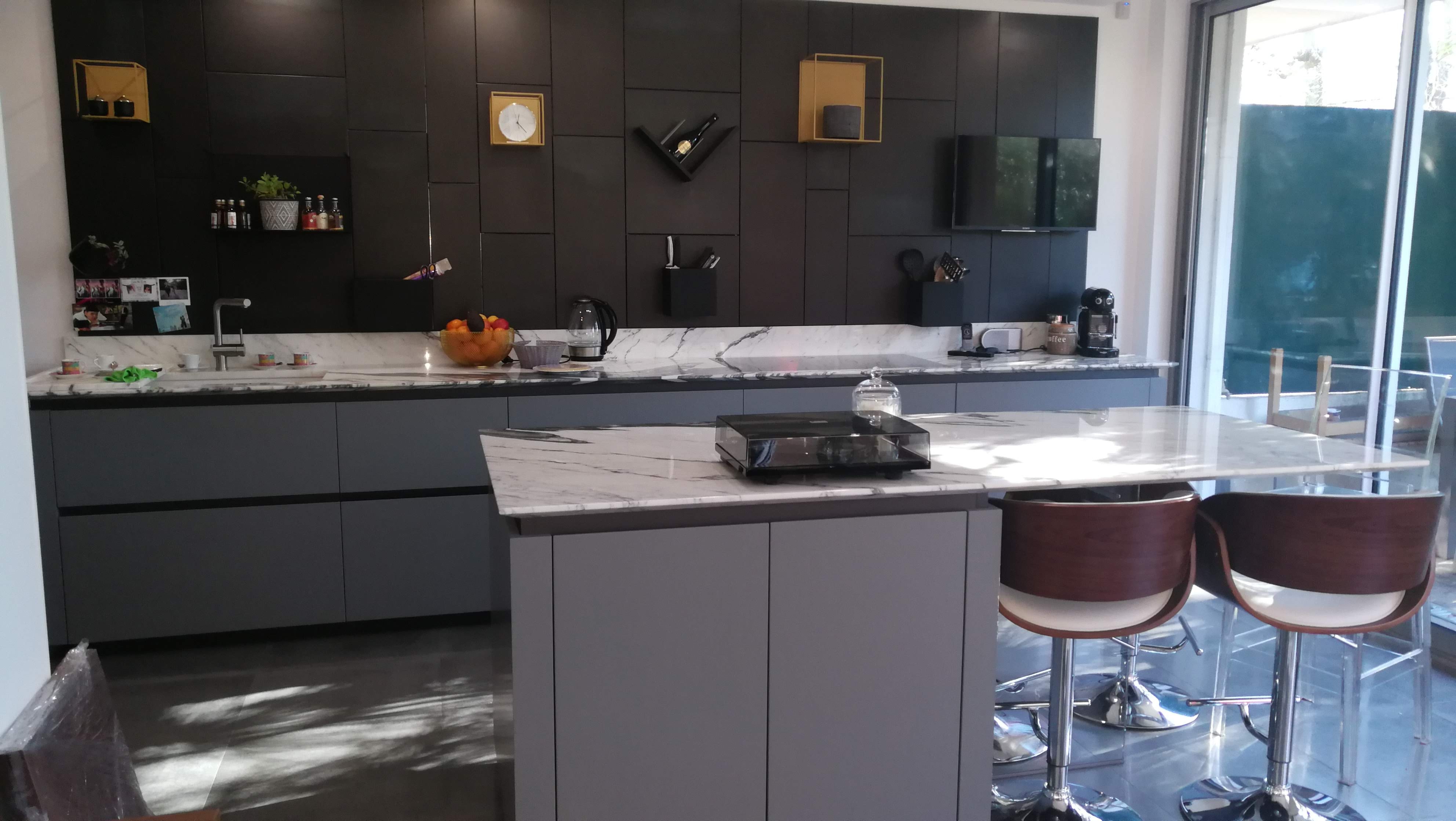 Cozinha com parede preta, bancada em marmore, ilha central e bancos em madeira escura