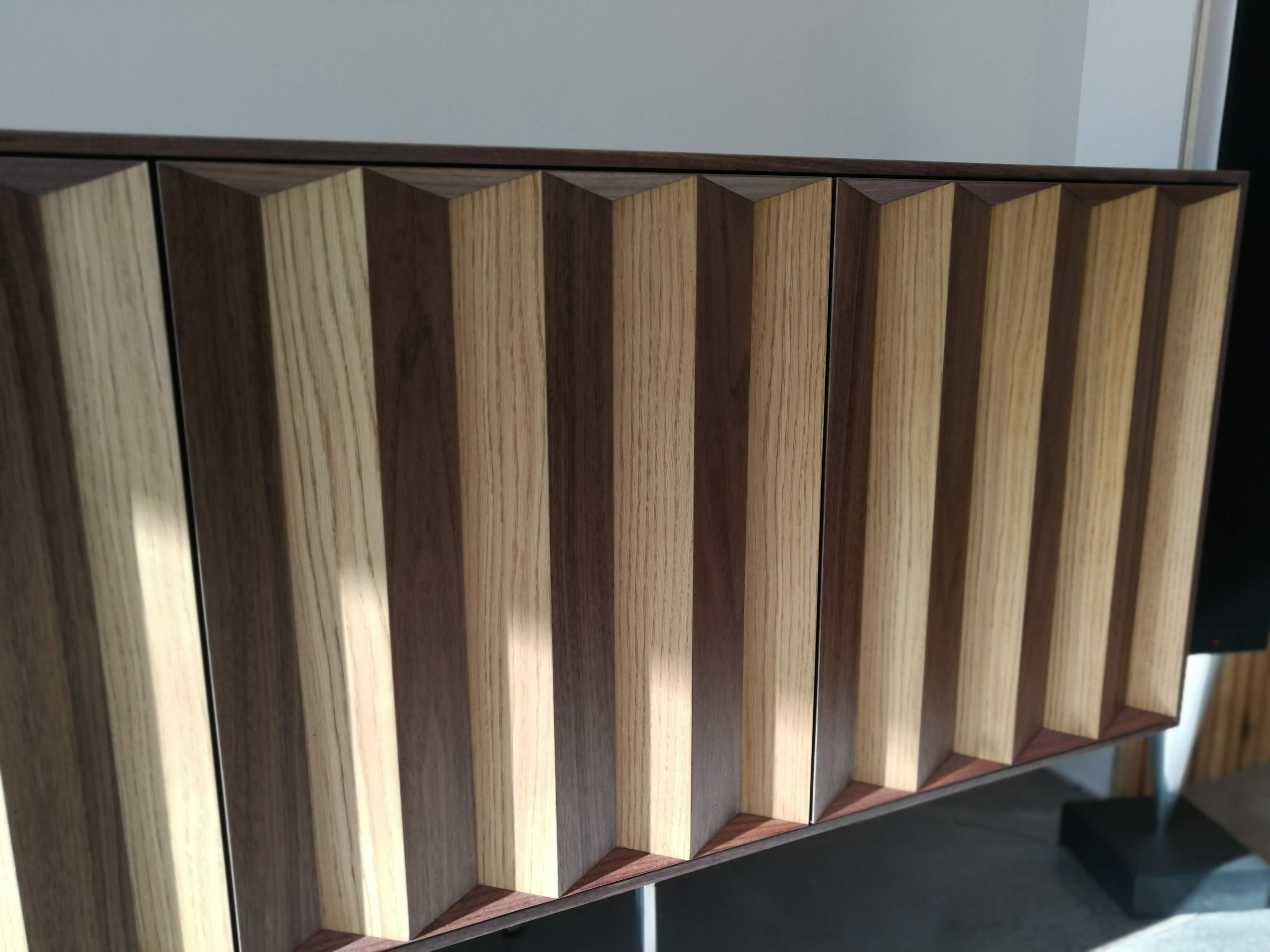 Pormenor frontal do aparador com ripas facetadas criando efeito tridimensional