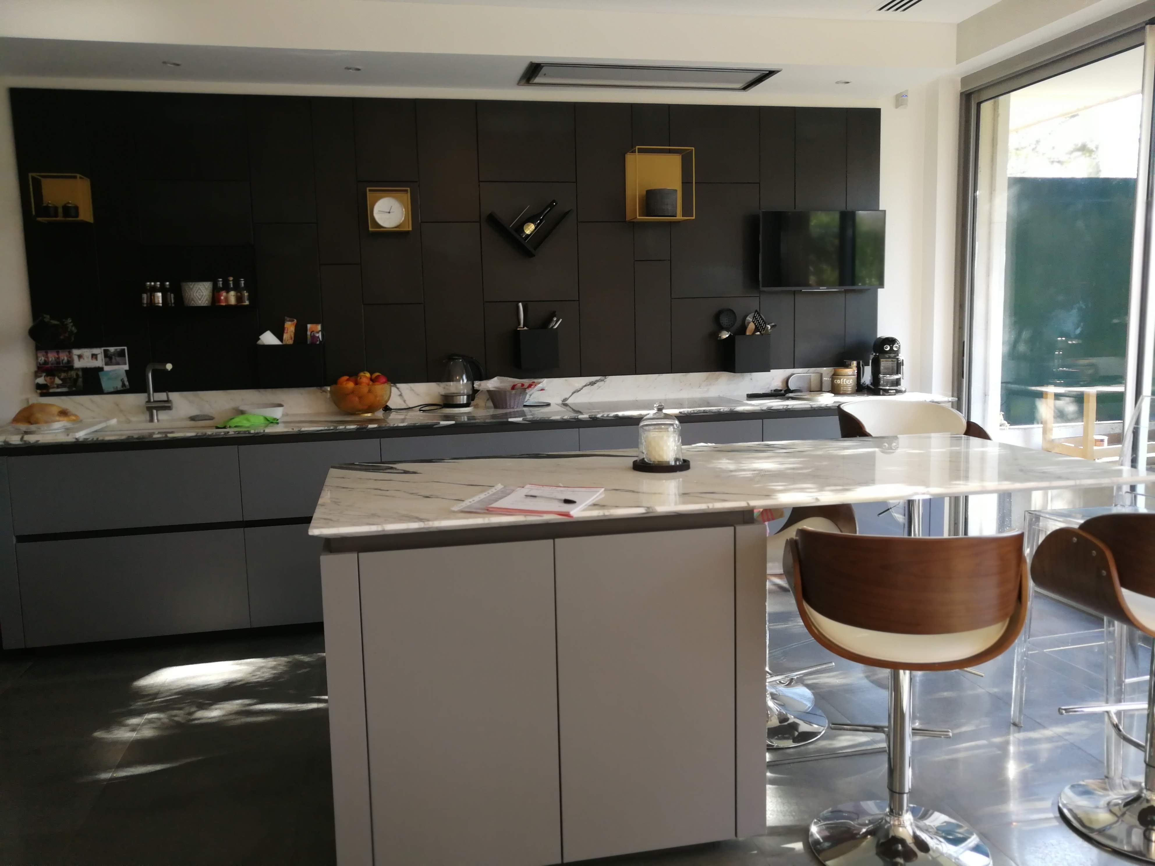 Cozinha com ilha central, parede preta com acessorios dourados e bancos em nogueira