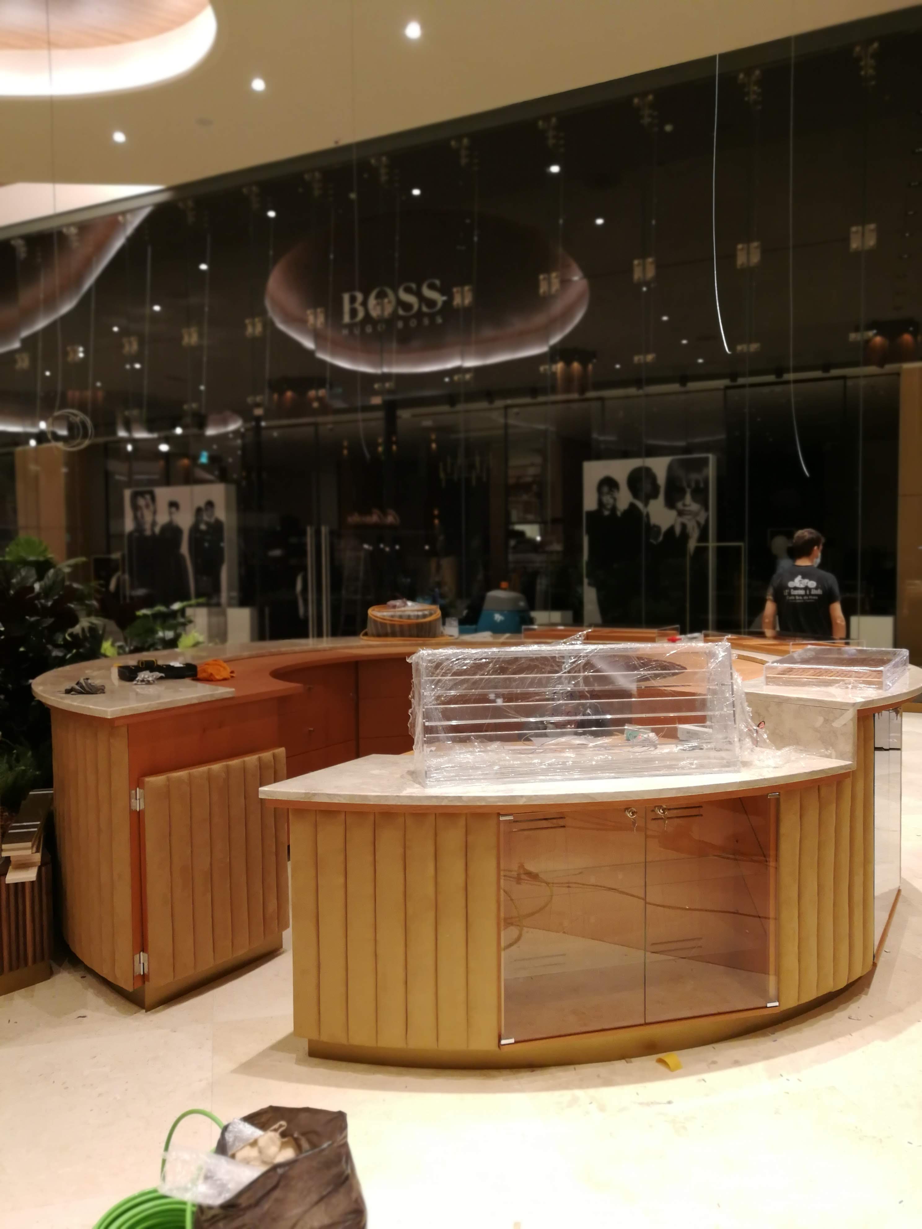 Vista lateral do balcao com paineis em madeira ripada, tampo em marmore e vitrinas em vidro curvado