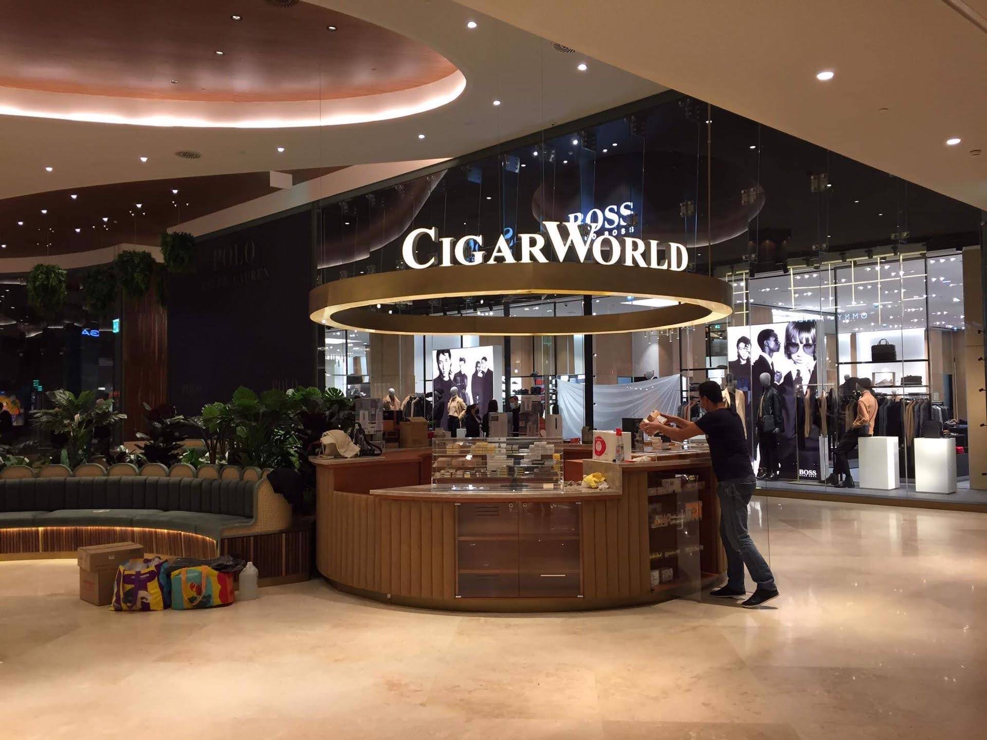 Vista ampla do quiosque CigarWorld integrado no ambiente premium do centro comercial com letreiro iluminado