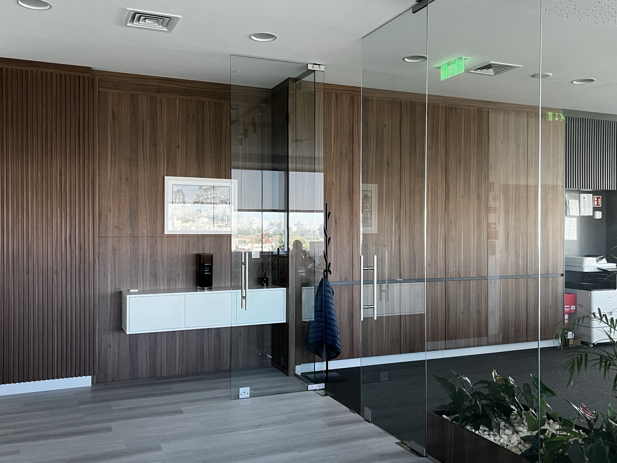 Corredor com parede revestida em nogueira, ripado vertical, modulo suspenso branco e porta em vidro