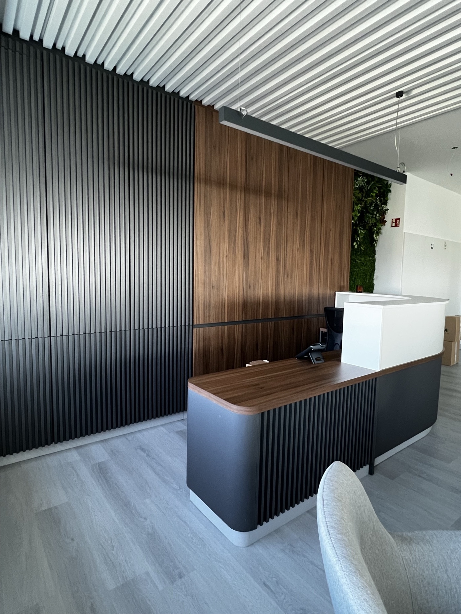 Vista superior do balcao de rececao com paineis ripados escuros, tampo em nogueira e jardim vertical ao fundo