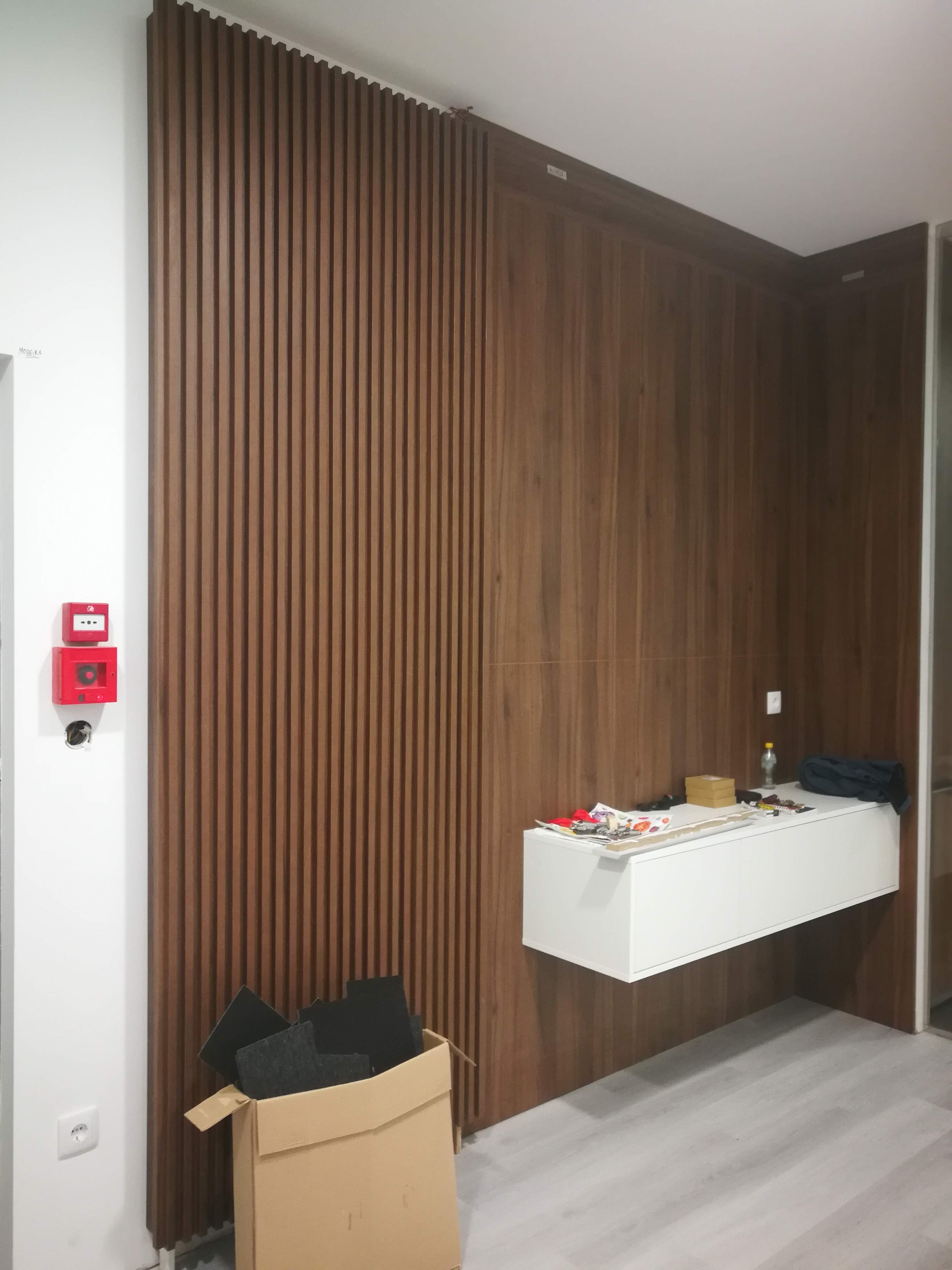 Parede de destaque com ripado vertical em nogueira e modulo suspenso lacado branco em fase de acabamento