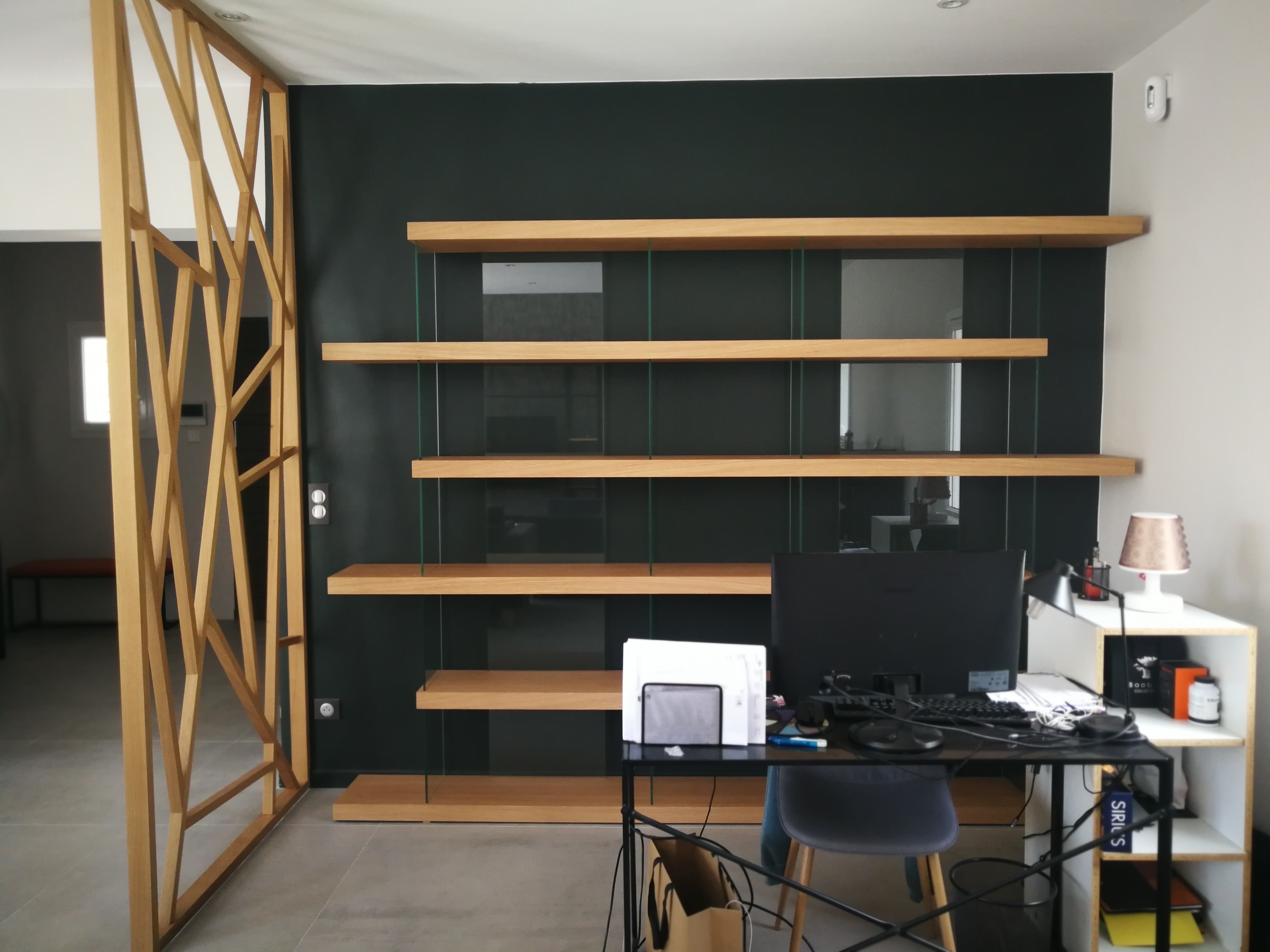 Escritorio com estante de prateleiras em carvalho sobre parede verde escura e divisoria geometrica em madeira