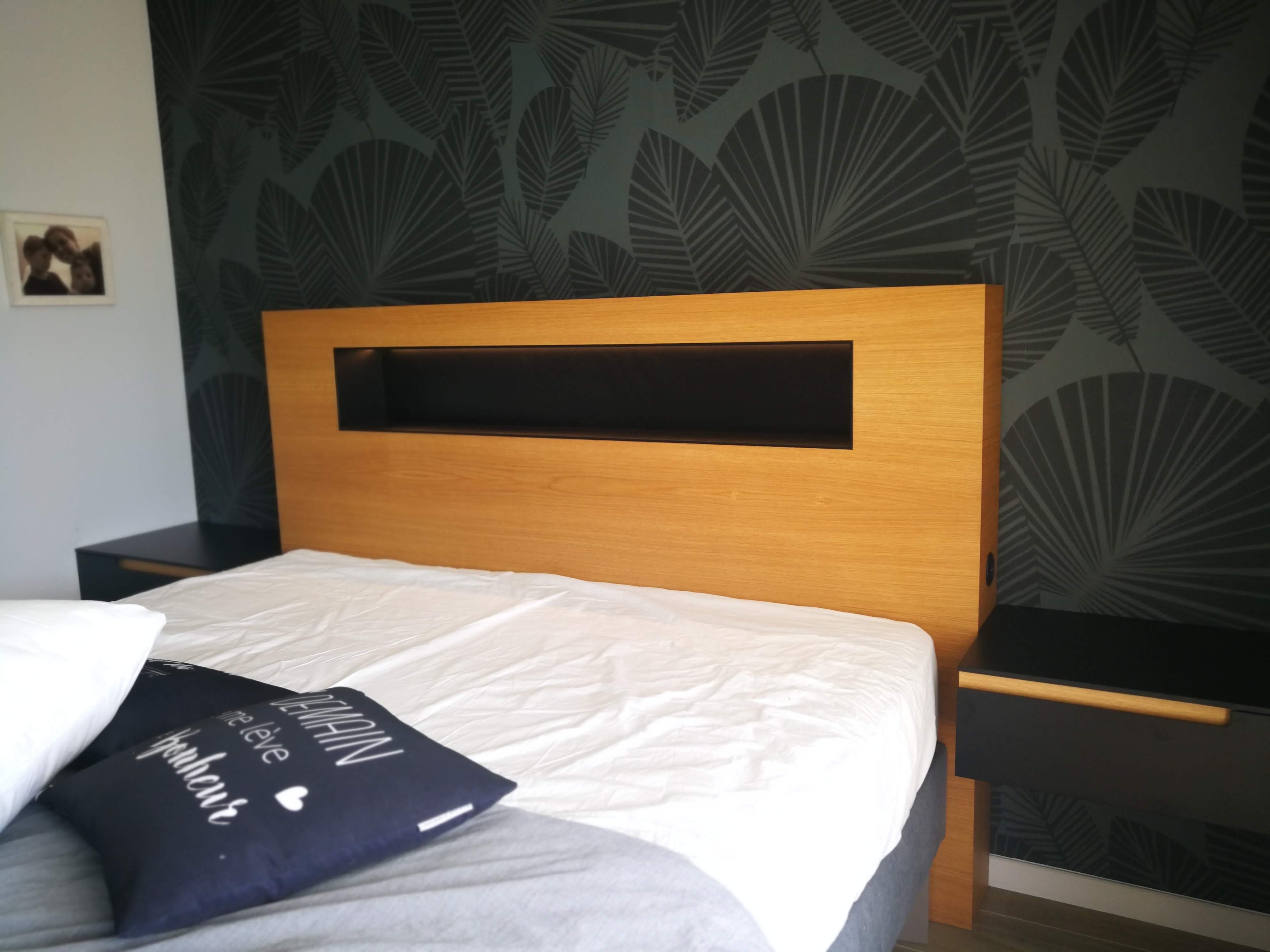 Quarto com cabeceira em carvalho com nicho preto iluminado e papel de parede tropical verde