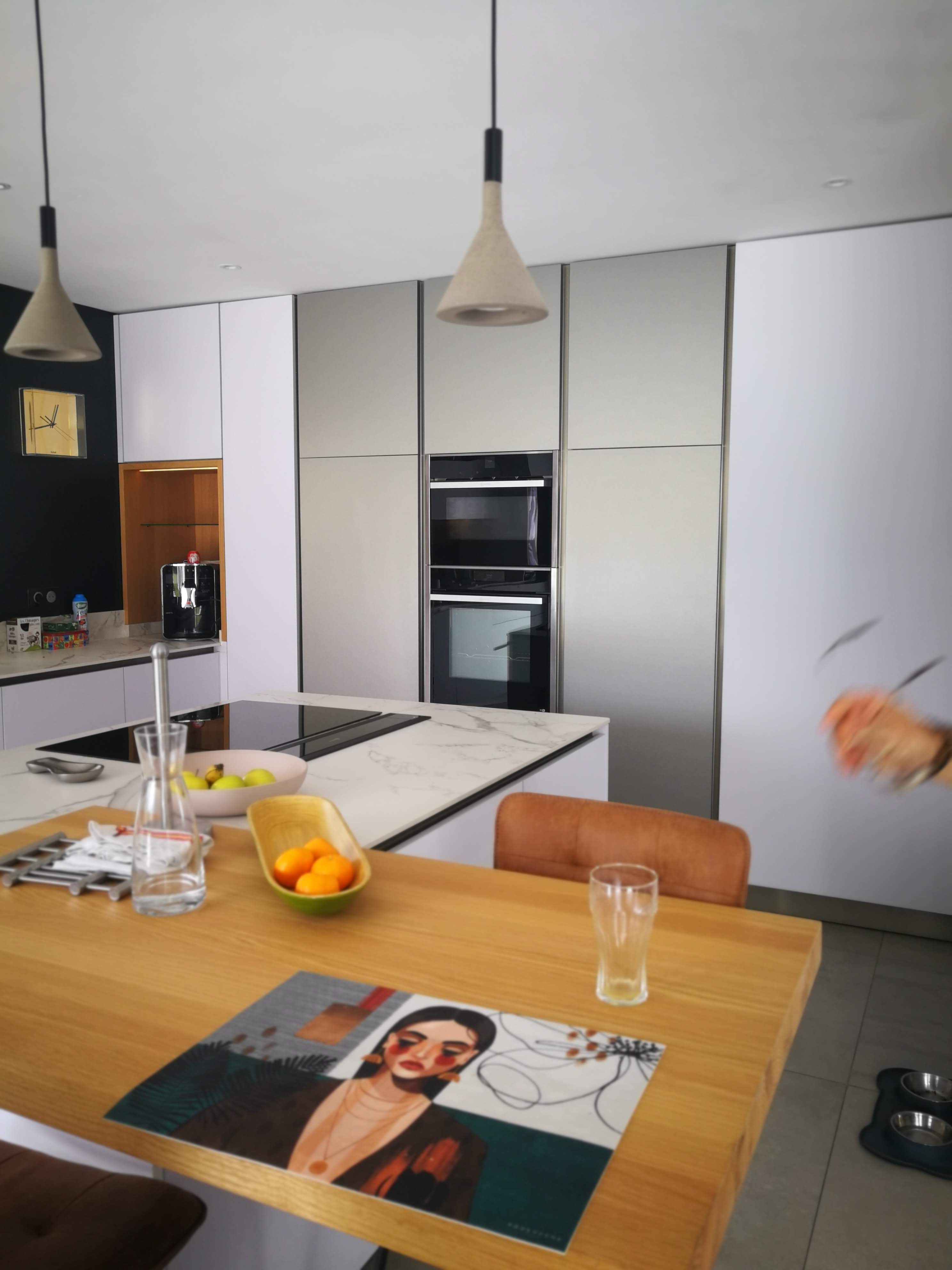 Cozinha com ilha em branco e marmore, mesa em carvalho com bancos em couro e fornos encastrados