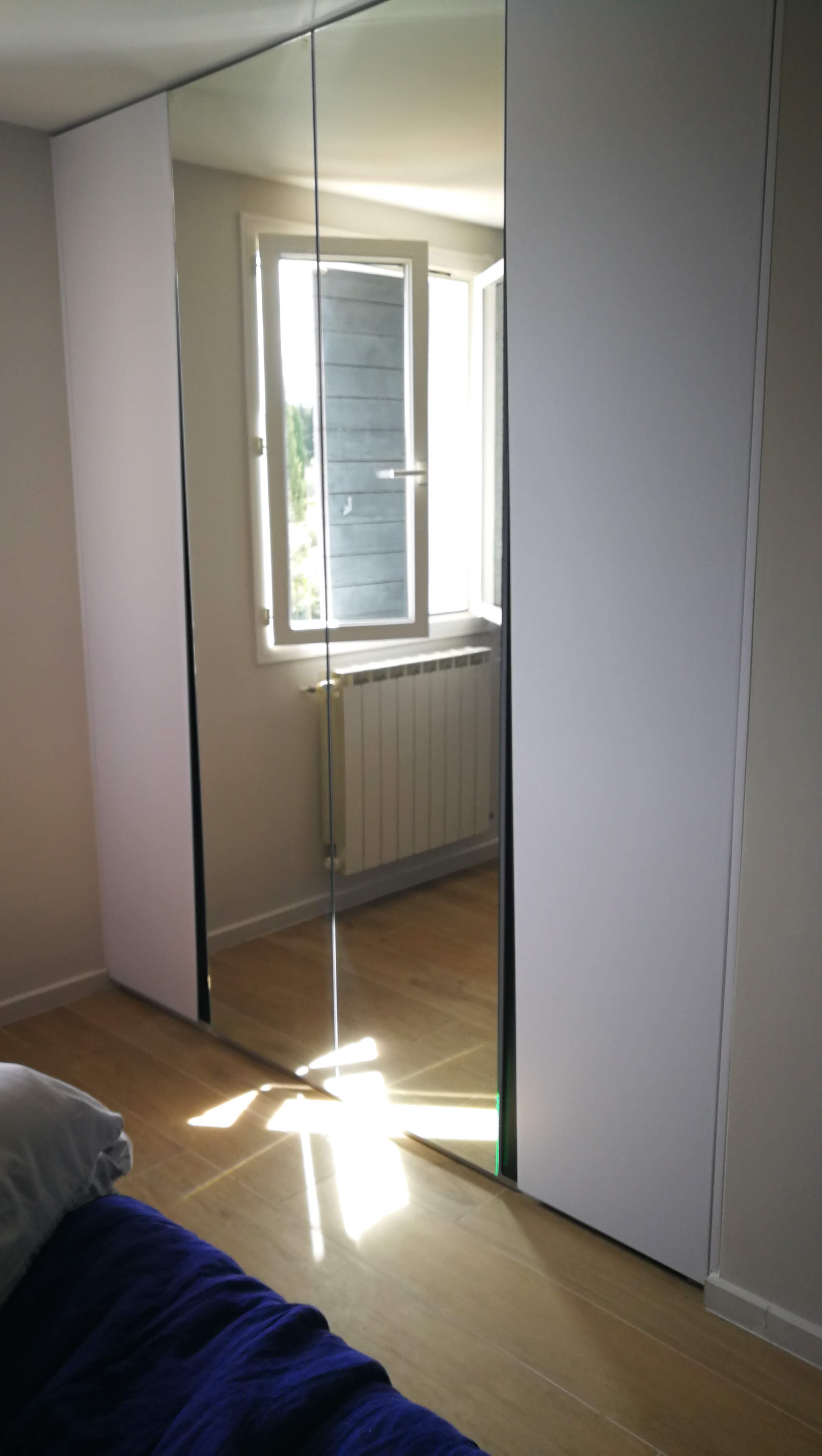 Roupeiro de portas espelhadas e paineis brancos em quarto com pavimento em madeira clara