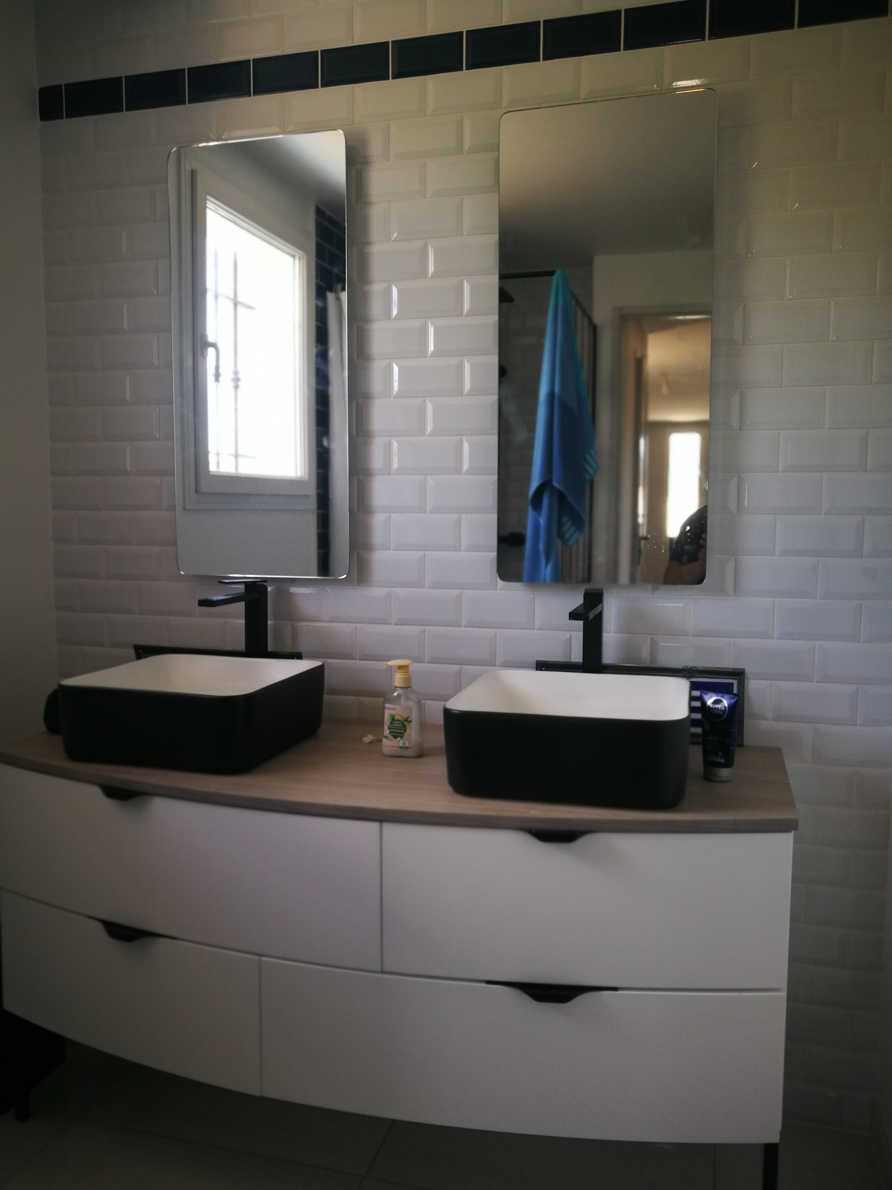 Casa de banho com duplo lavatorio preto e branco sobre movel branco, azulejo metro e torneiras pretas