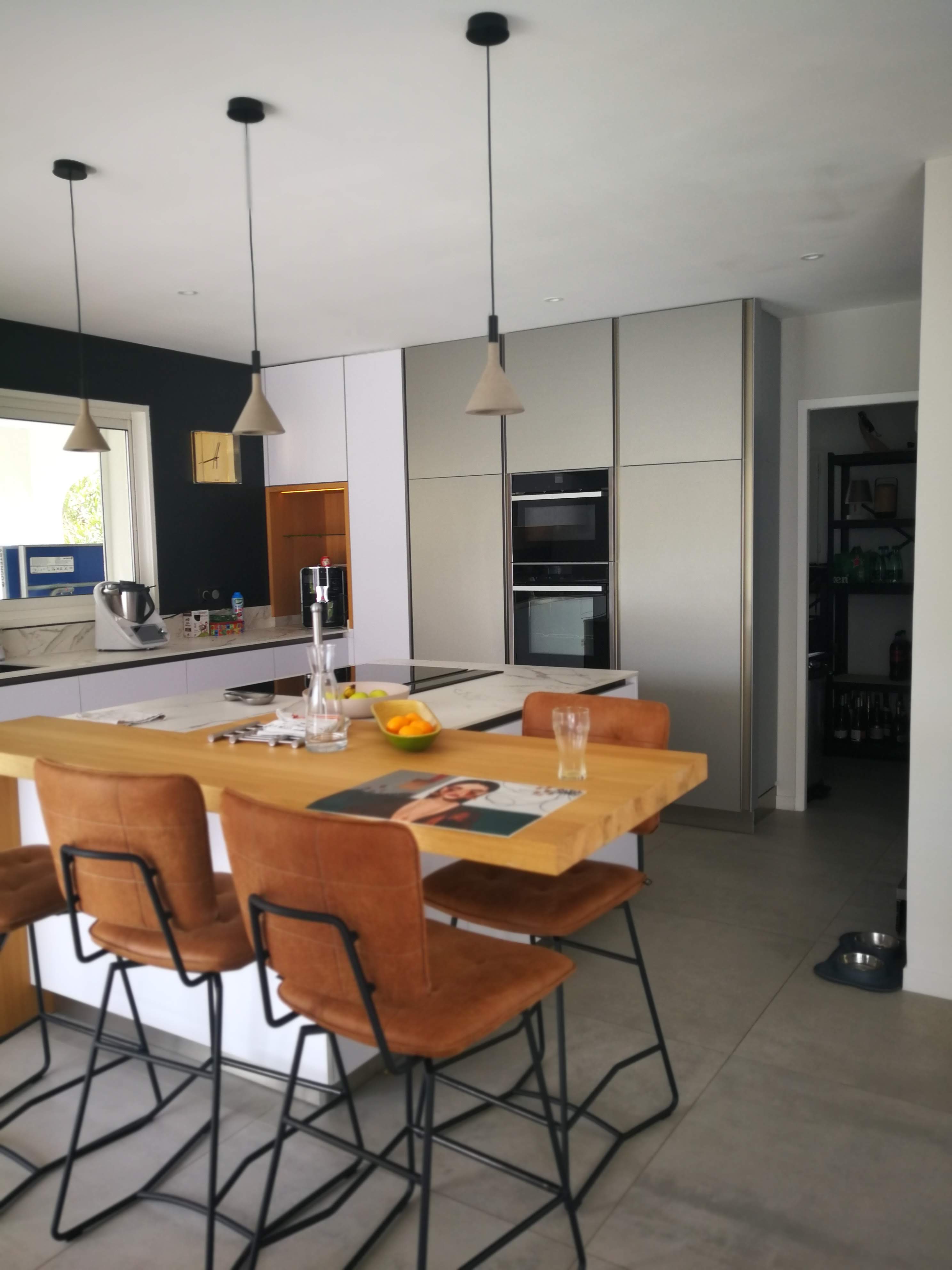 Cozinha com ilha, bancada em carvalho, bancos em couro e armarios coluna cinza com eletrodomesticos