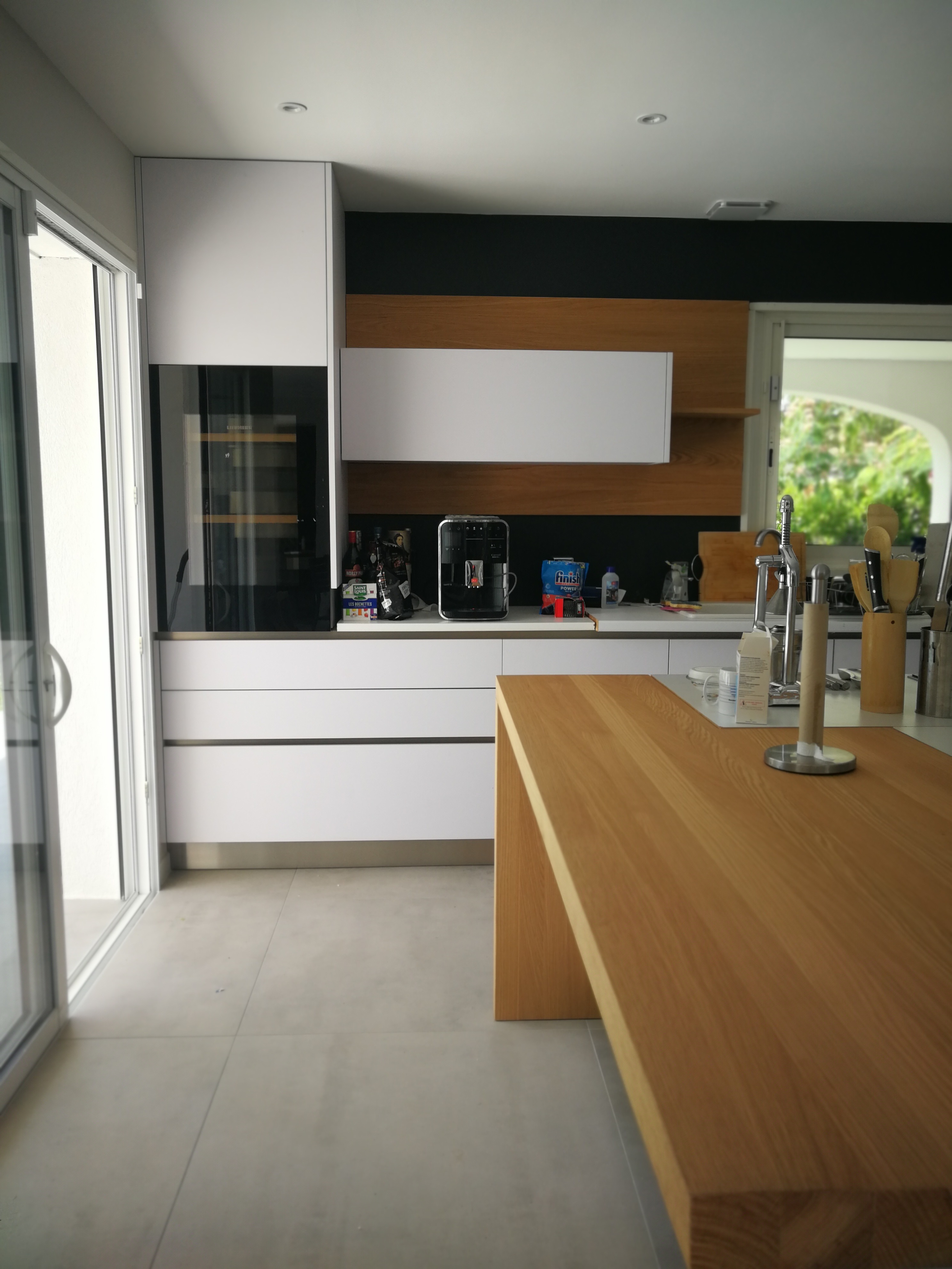 Cozinha com armarios brancos, bancada em carvalho e parede de fundo em preto com painel de madeira