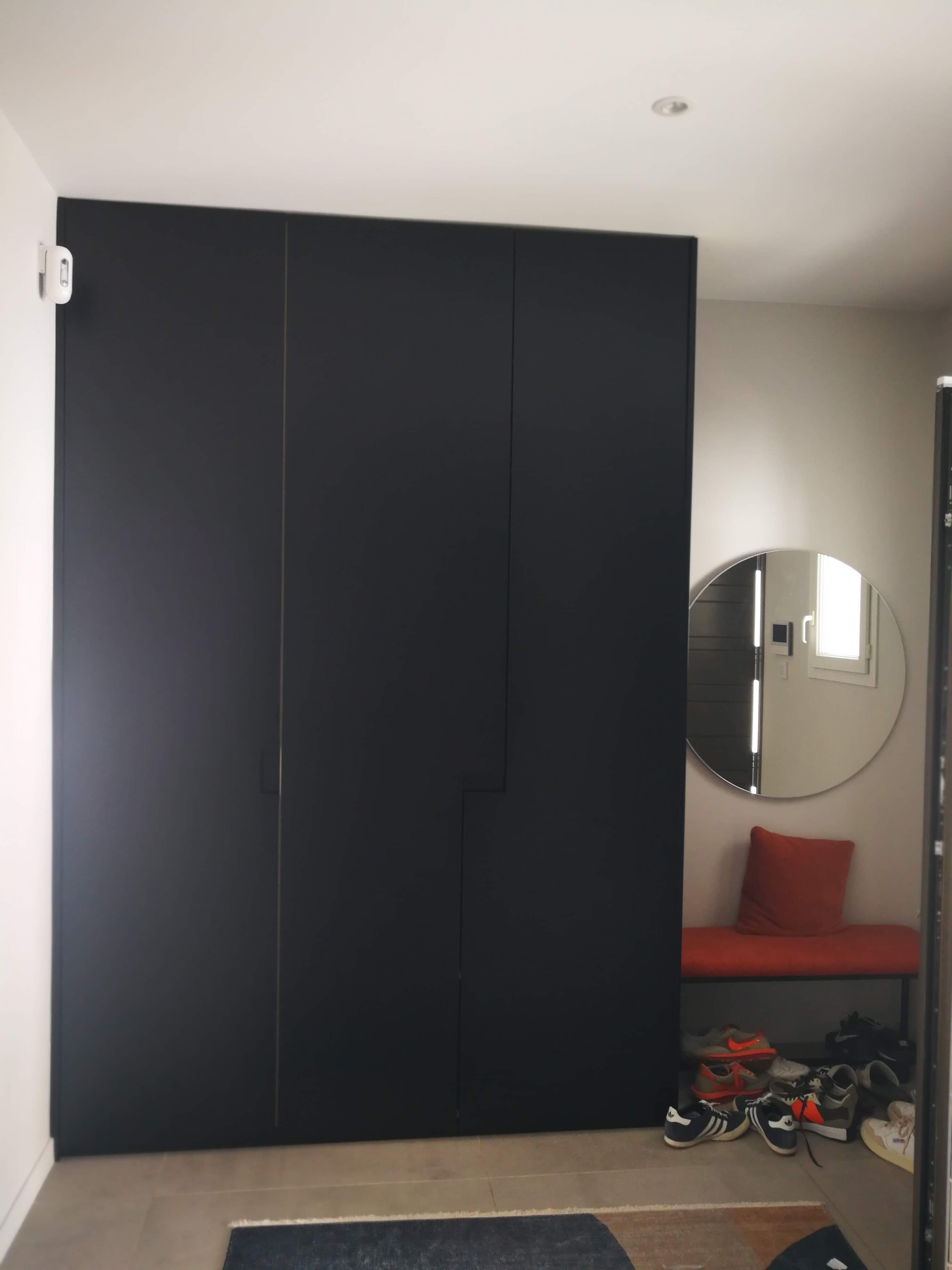 Entrada com armario preto mate de tres portas, espelho redondo e banco com almofada vermelha