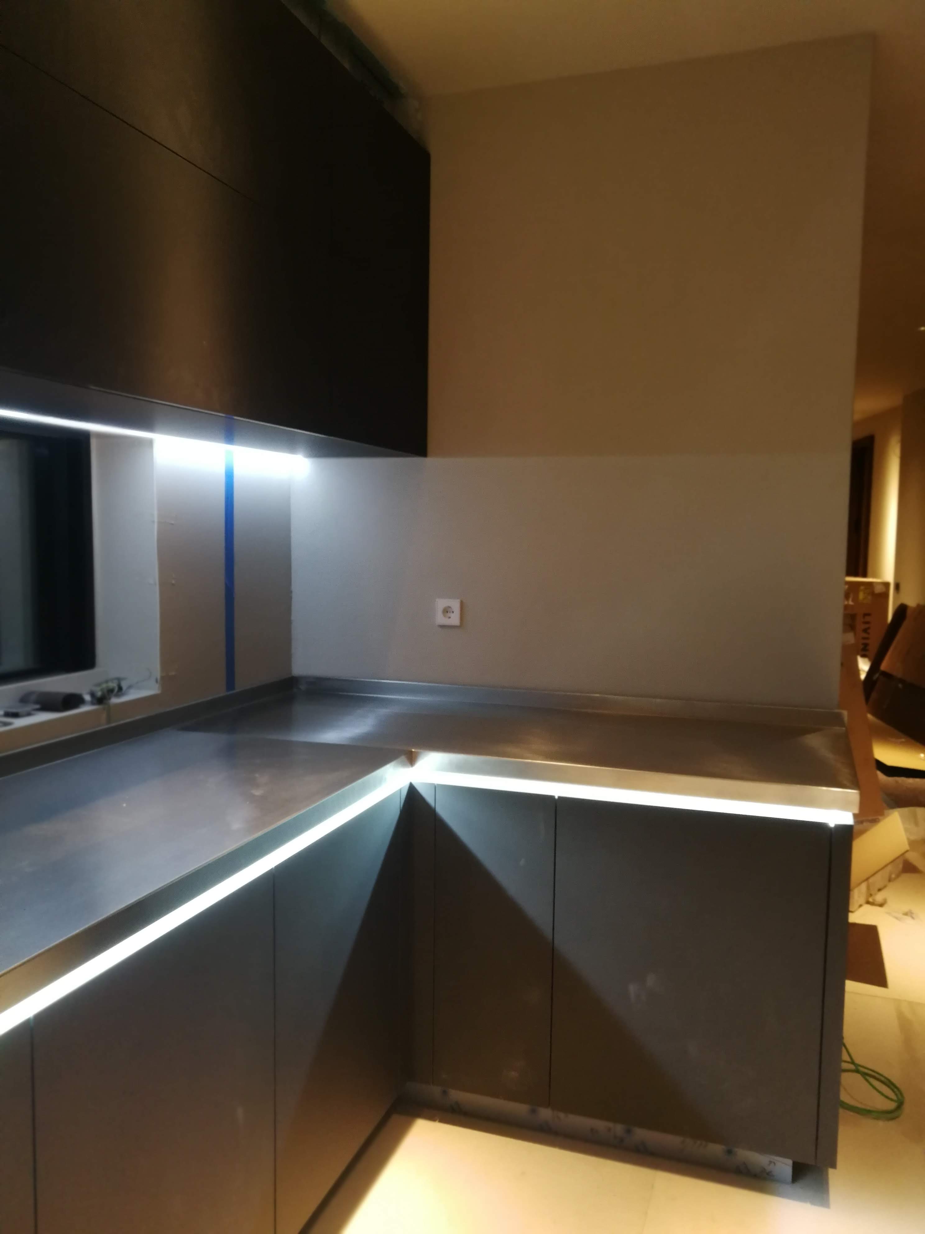 Cozinha em fase de acabamento com armarios e bancada em inox escuro e iluminacao LED