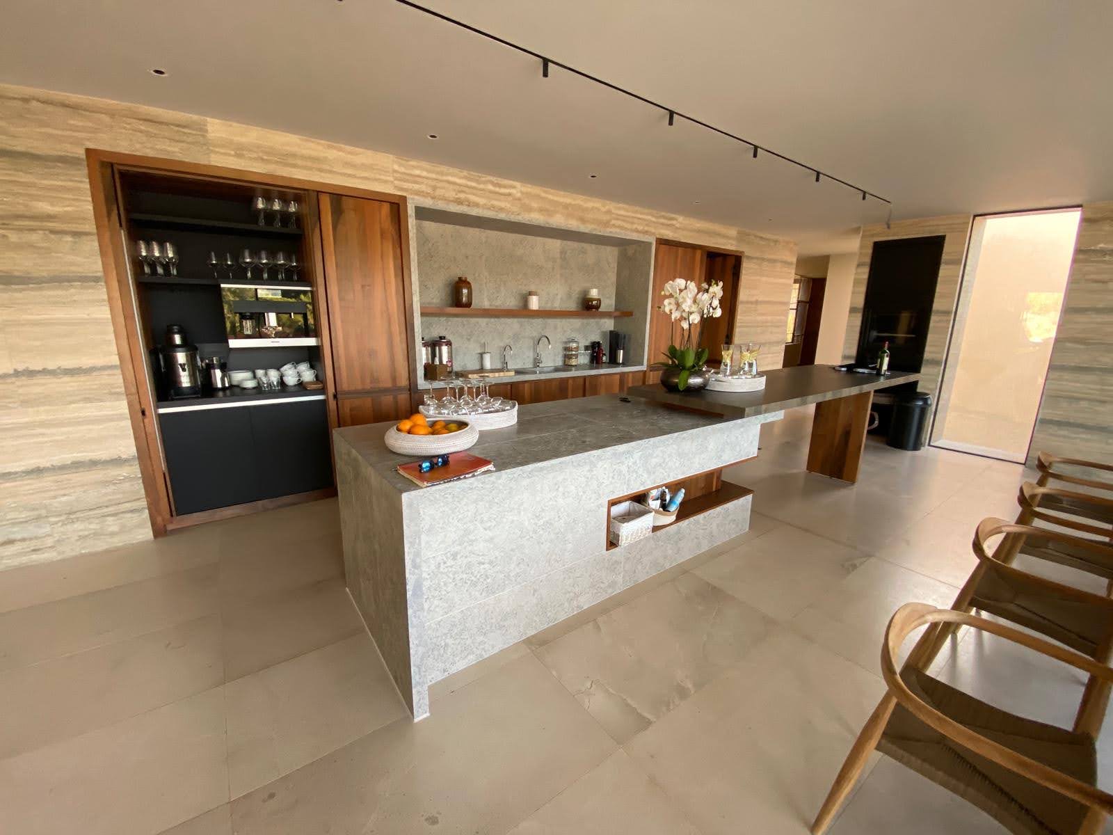 Cozinha finalizada com ilha em pedra cinza, bancada em nogueira, portas de correr e orquideas