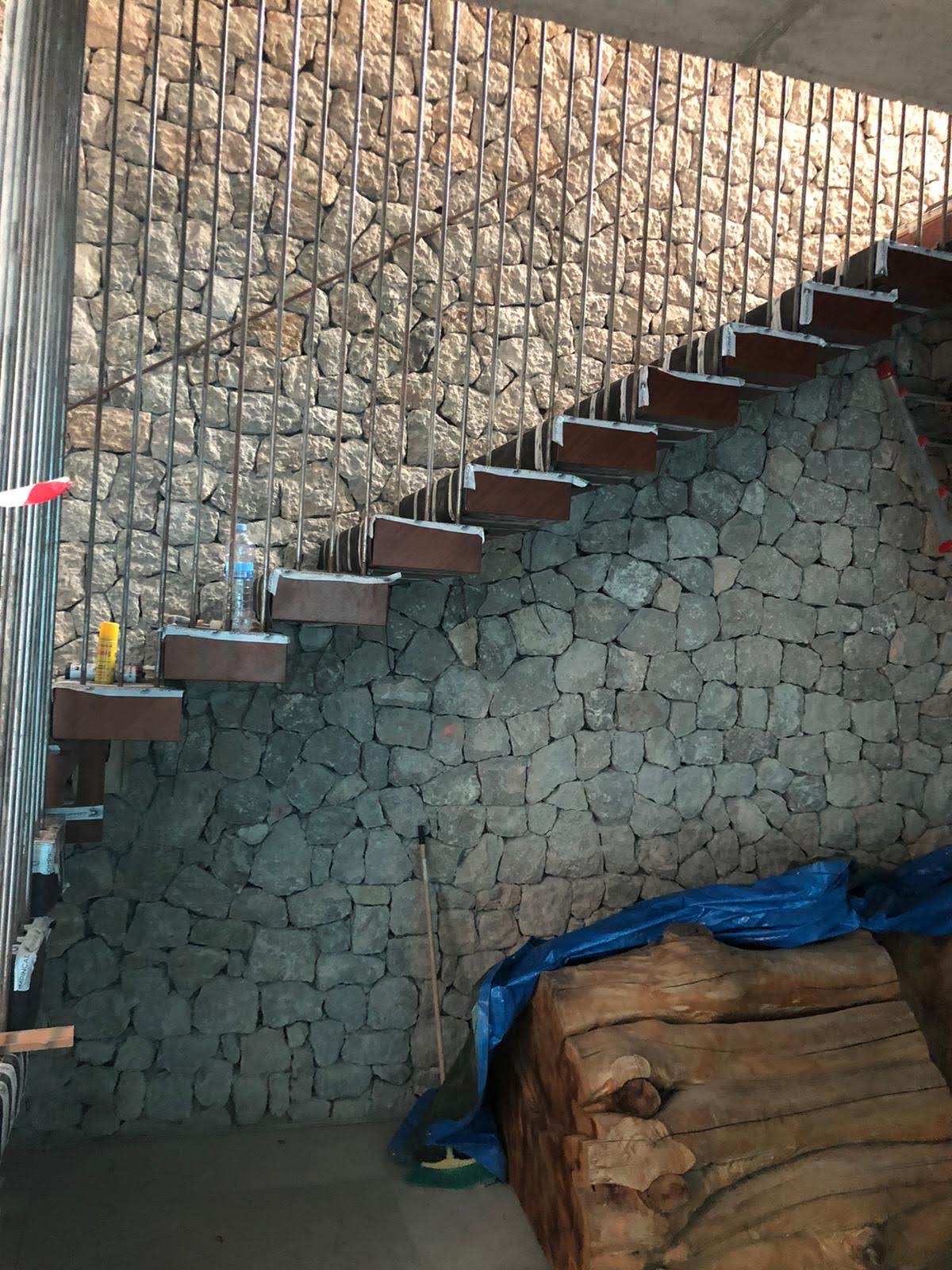 Escadaria em construcao com degraus em aco corten, parede de pedra natural e tronco esculpido