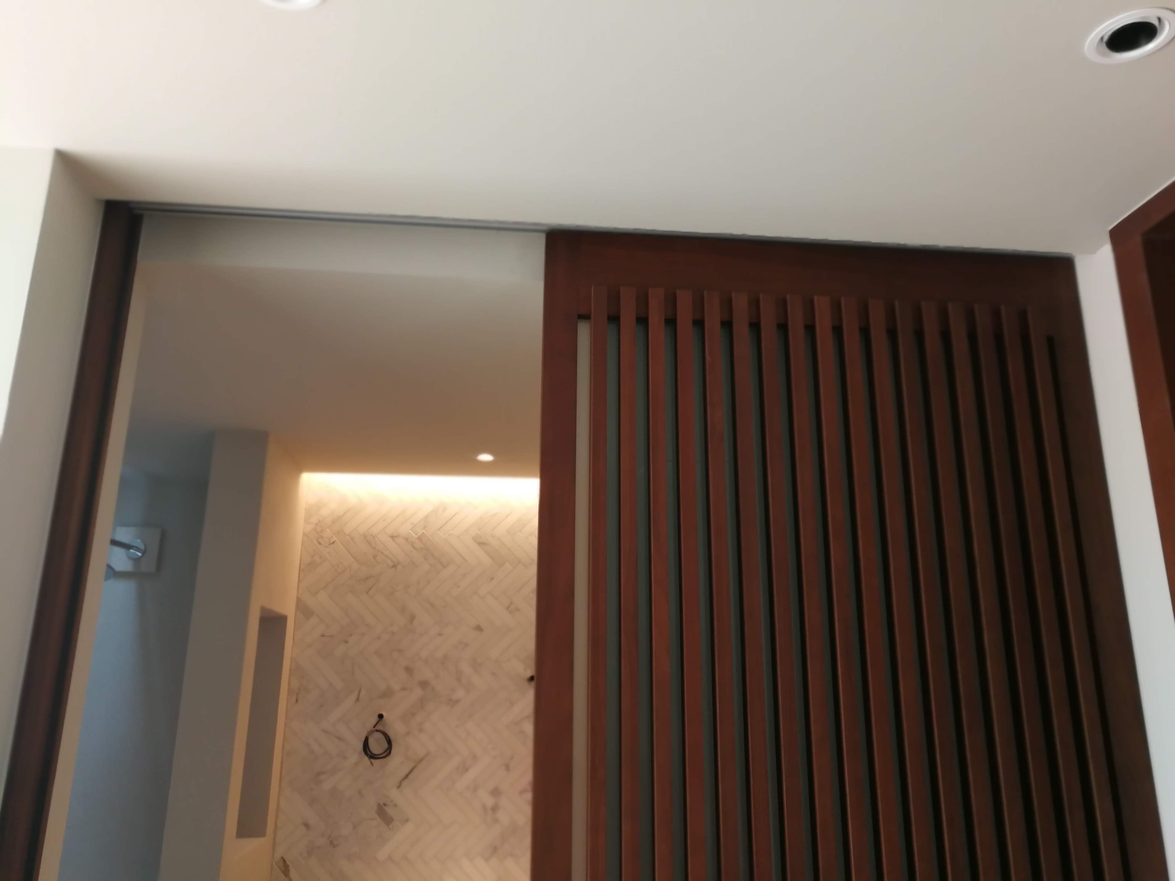 Divisoria de casa de banho com porta em ripas de madeira escura e azulejo espinha de peixe