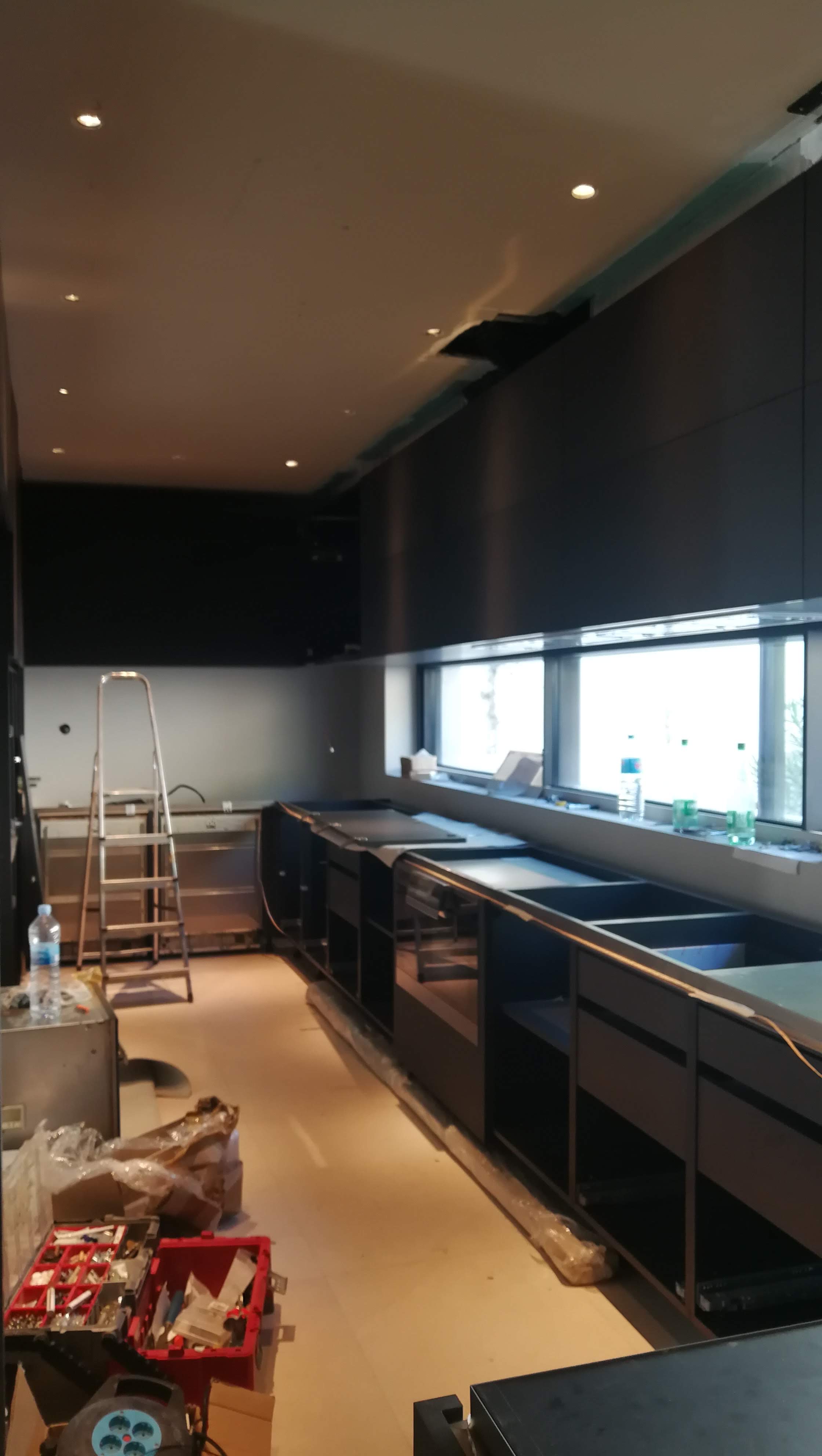 Cozinha escura em fase de montagem com armarios pretos e bancadas em inox
