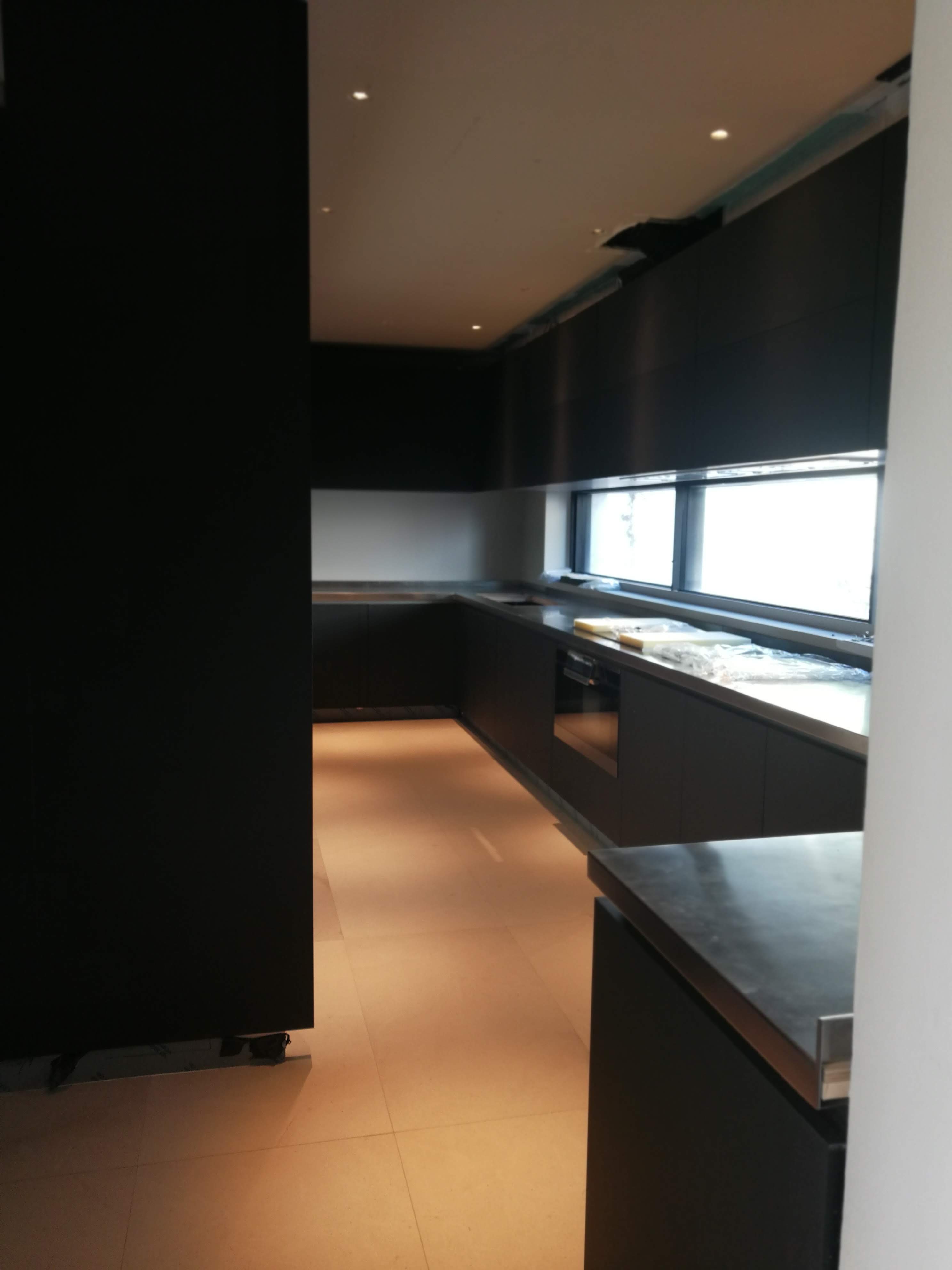 Cozinha escura em fase de acabamento com armarios pretos mate e bancada em aco