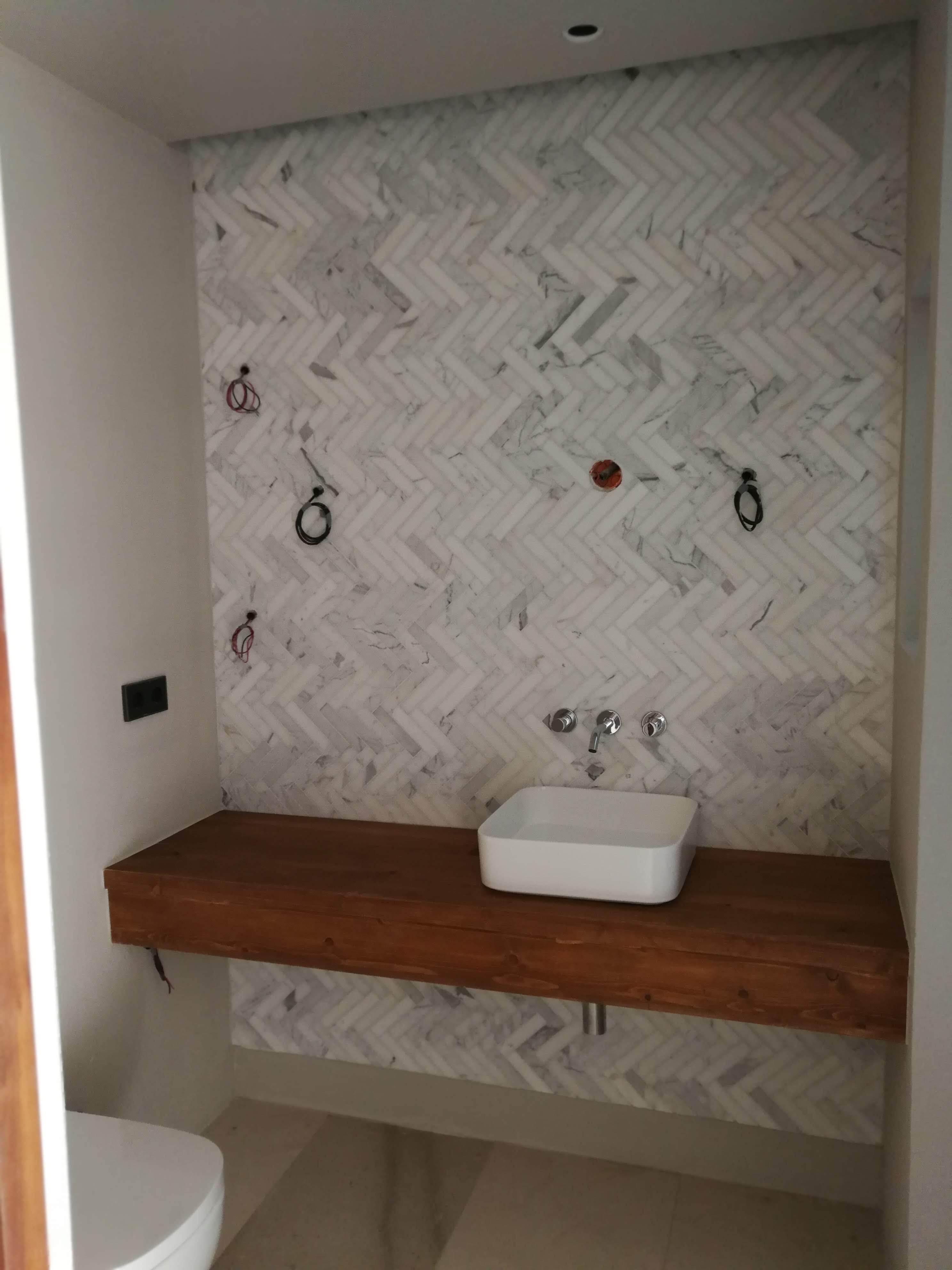 Casa de banho com lavatorio branco sobre bancada em madeira e azulejo espinha de peixe em marmore