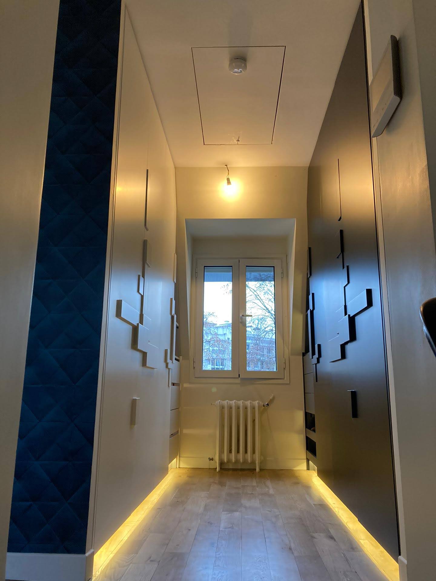 Closet estreito com armarios brancos, puxadores escalonados e parede em veludo azul-petroleo