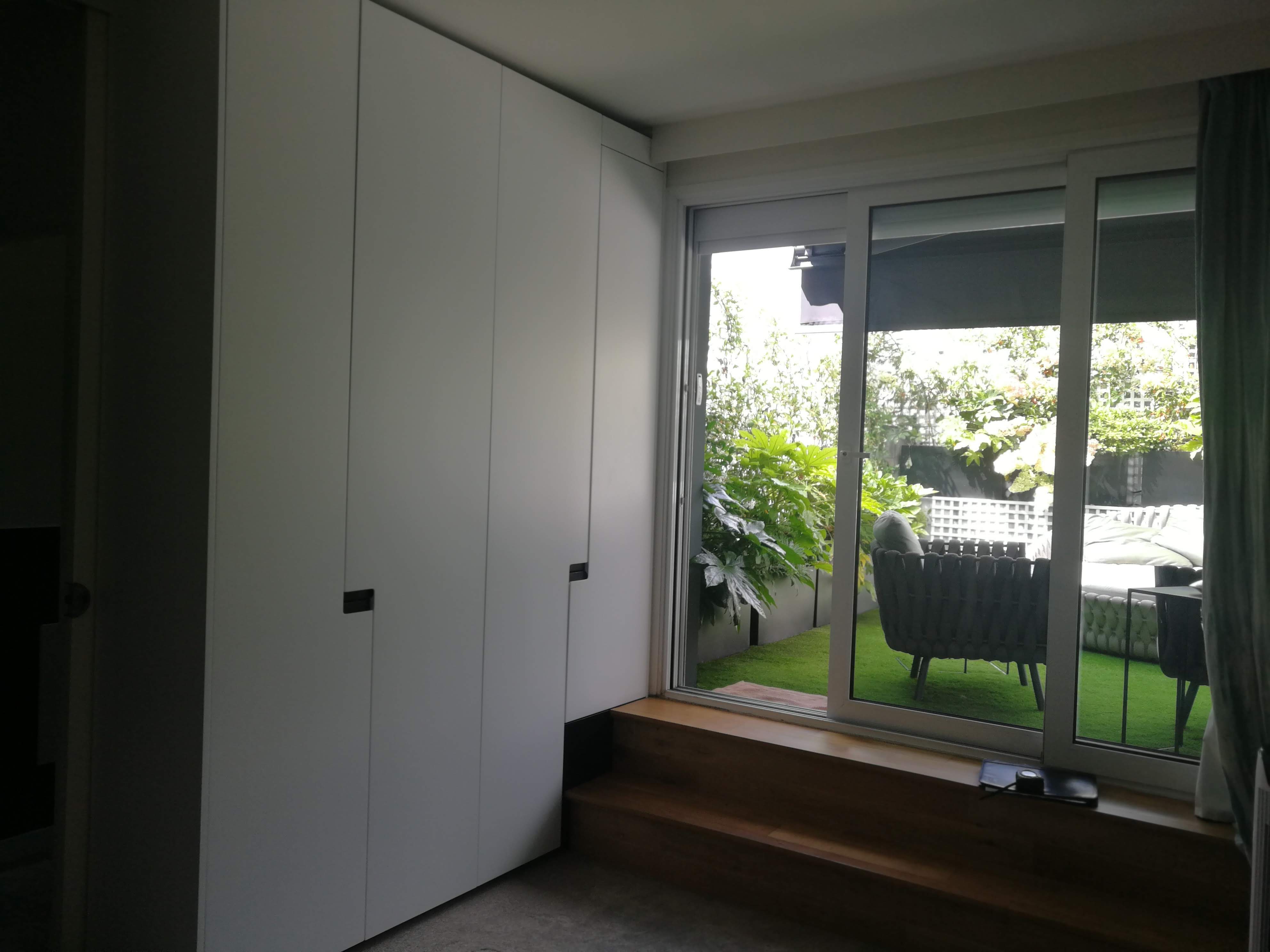 Quarto com armario branco junto a porta de correr em vidro com vista para terraco com relva