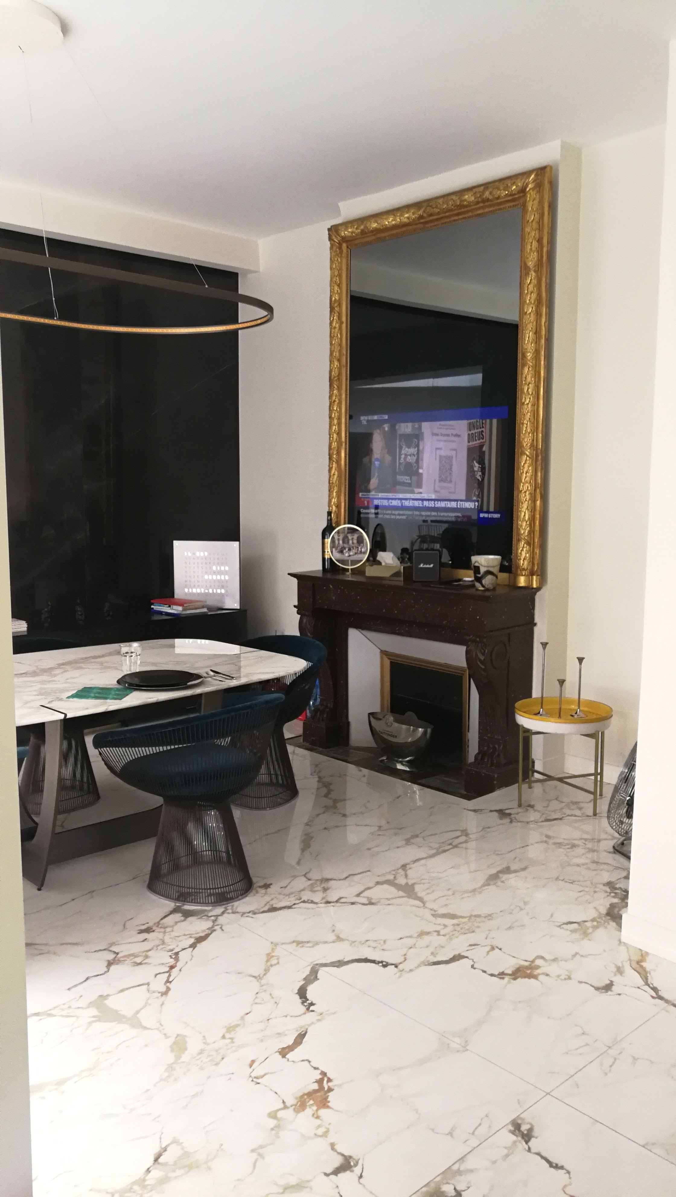 Sala de jantar com mesa redonda em marmore, cadeiras Platner, lareira com espelho dourado e candeeiro circular