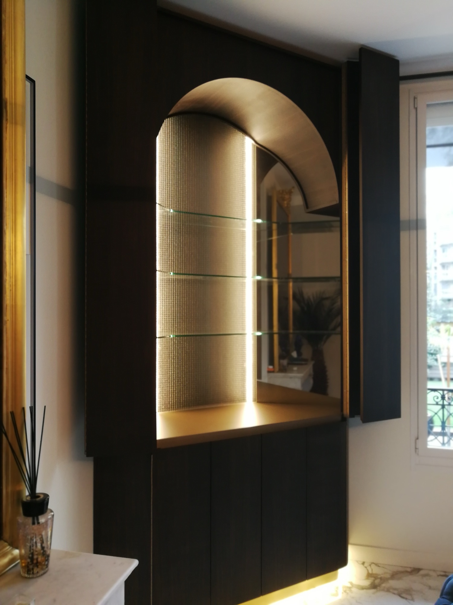 Outro angulo da vitrina em arco dourado com prateleiras de vidro no movel de madeira escura