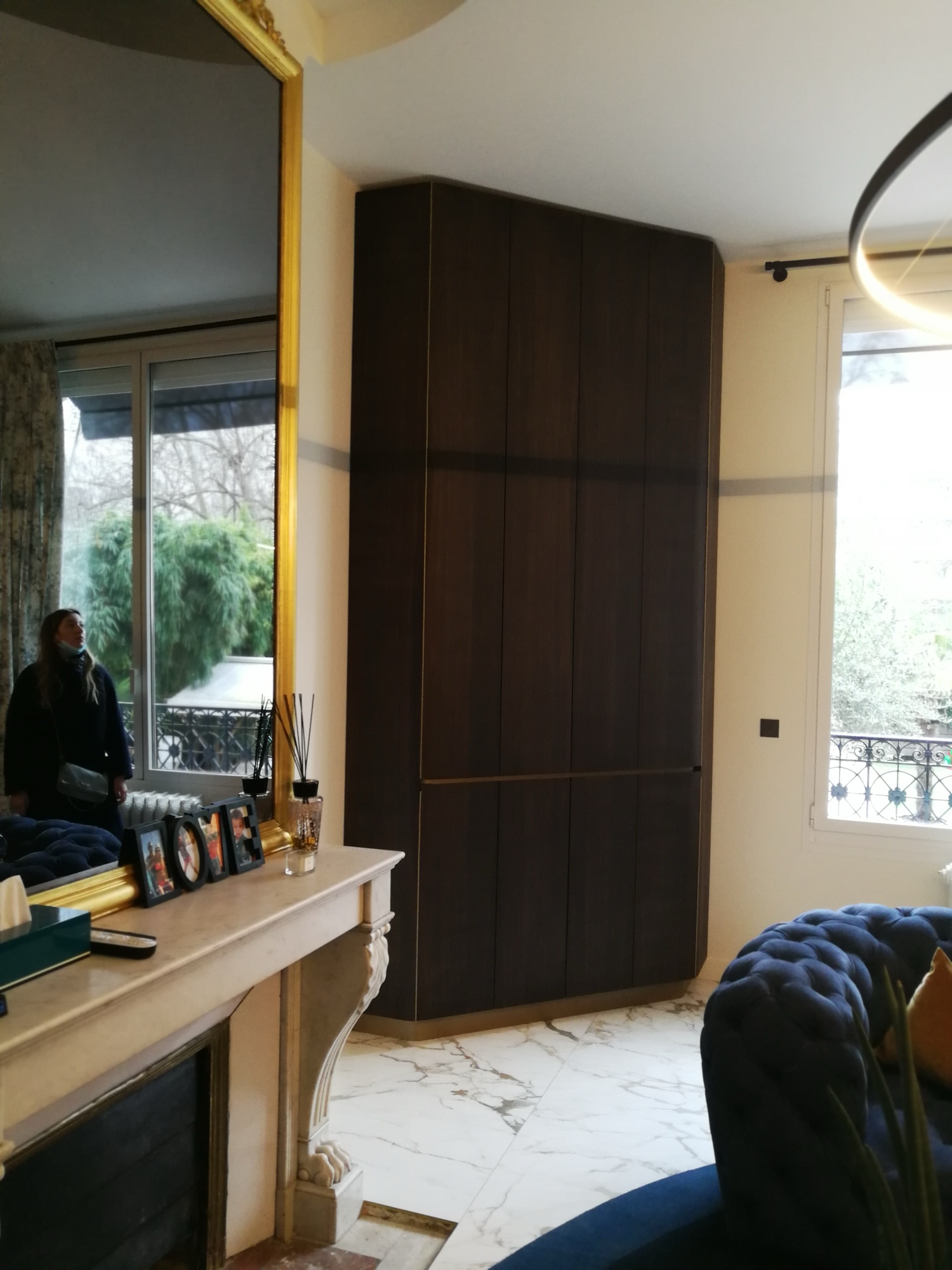 Vista geral da sala com armario em madeira escura, janela francesa, espelho dourado e sofa Chesterfield