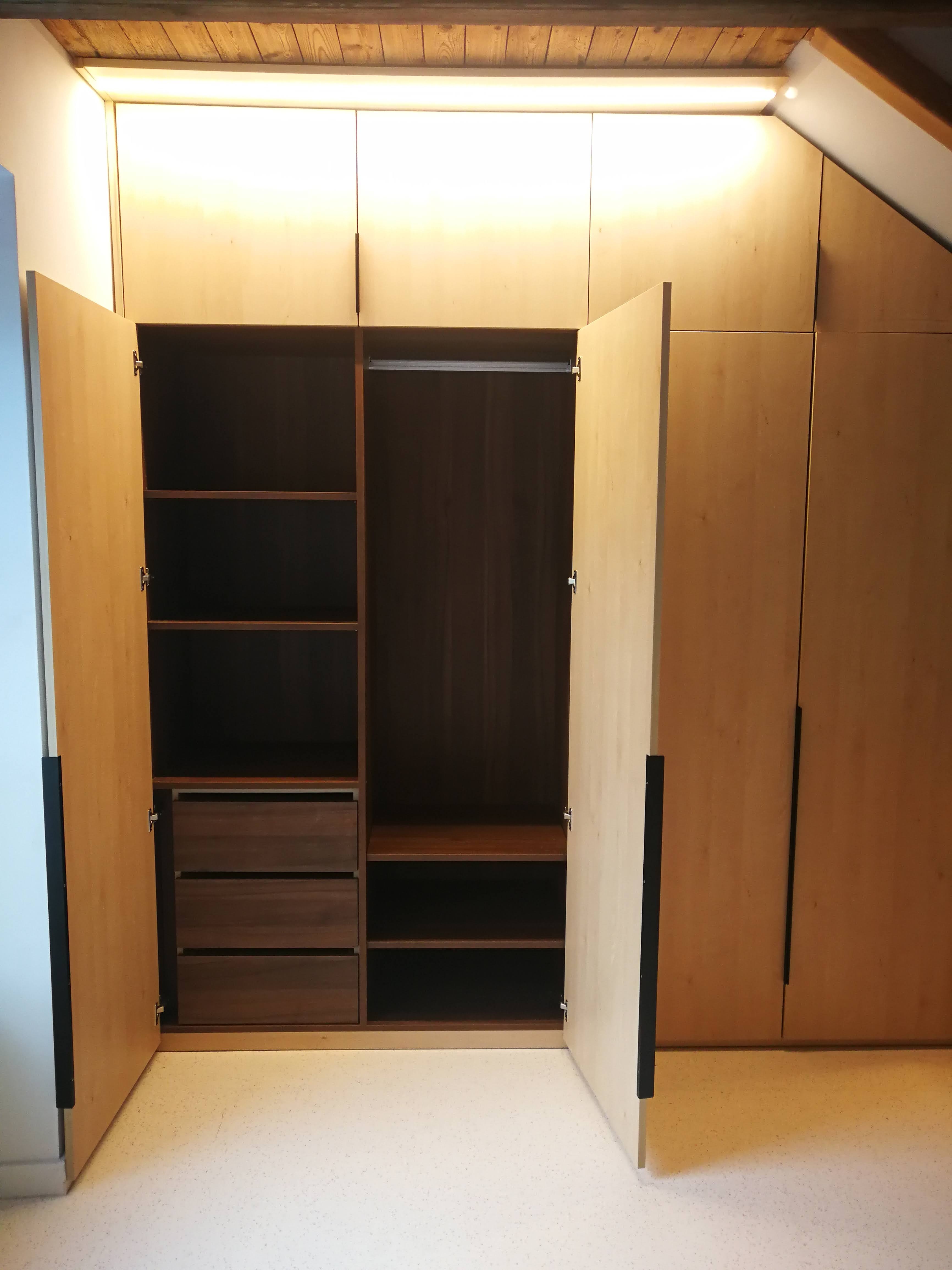 Interior de armario embutido em madeira clara com prateleiras, varoes e gavetas em nogueira e vigas a vista